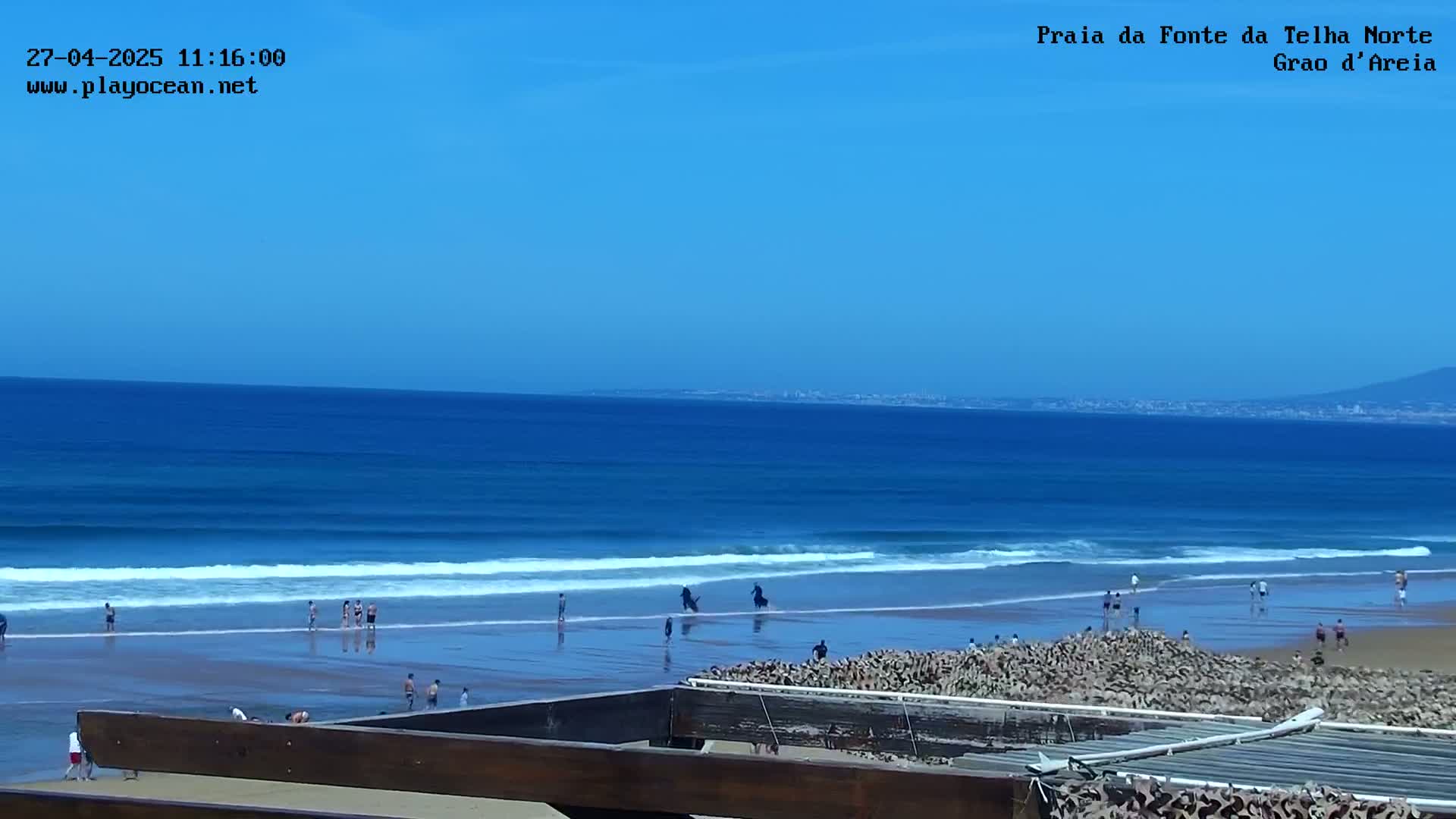 A sandy beach with people enjoying the ocean under a clear blue sky.