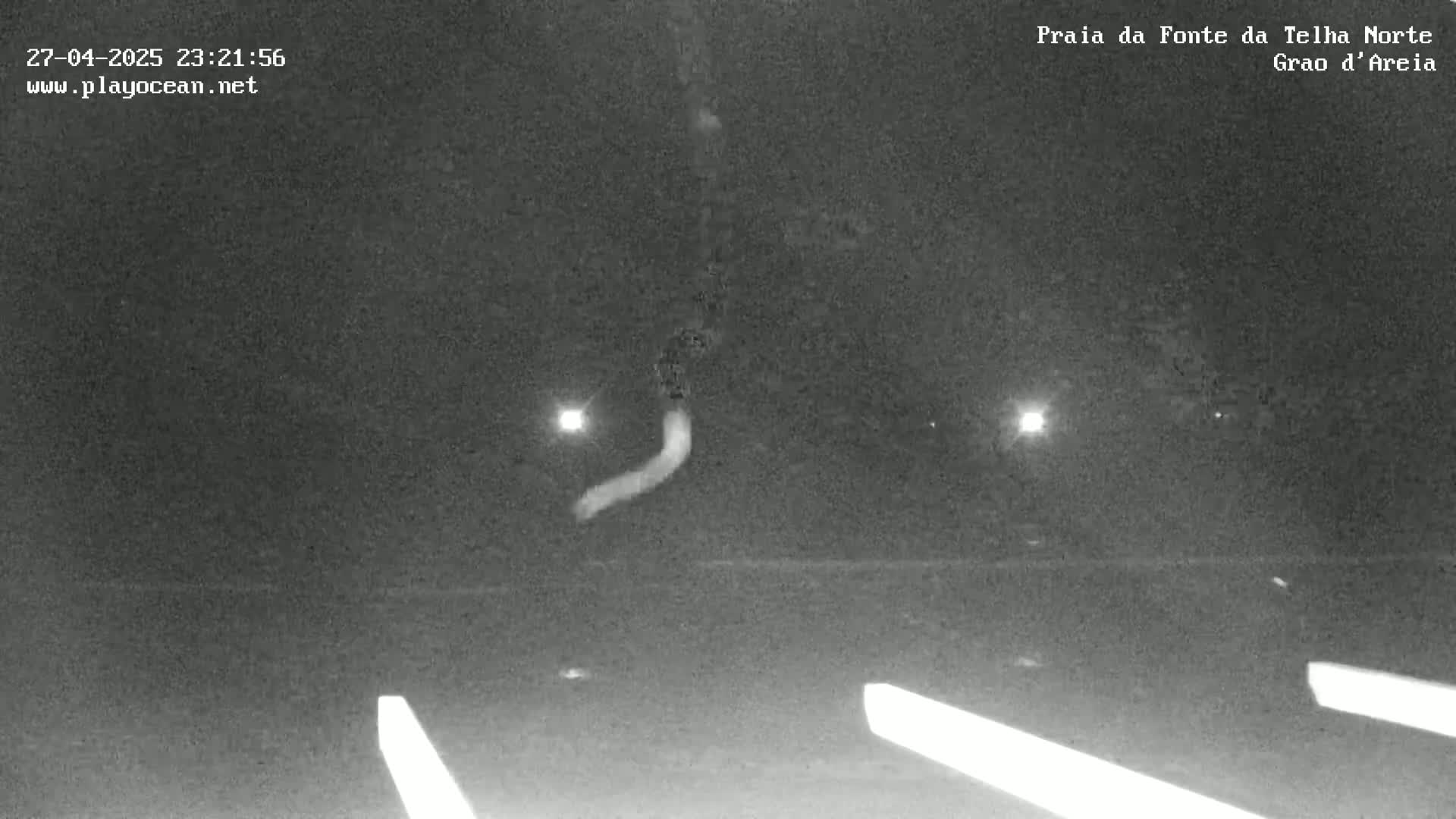 A nighttime, low-light view of a road with faint white lane markings, showing a blurry, light-colored object moving in the distance.