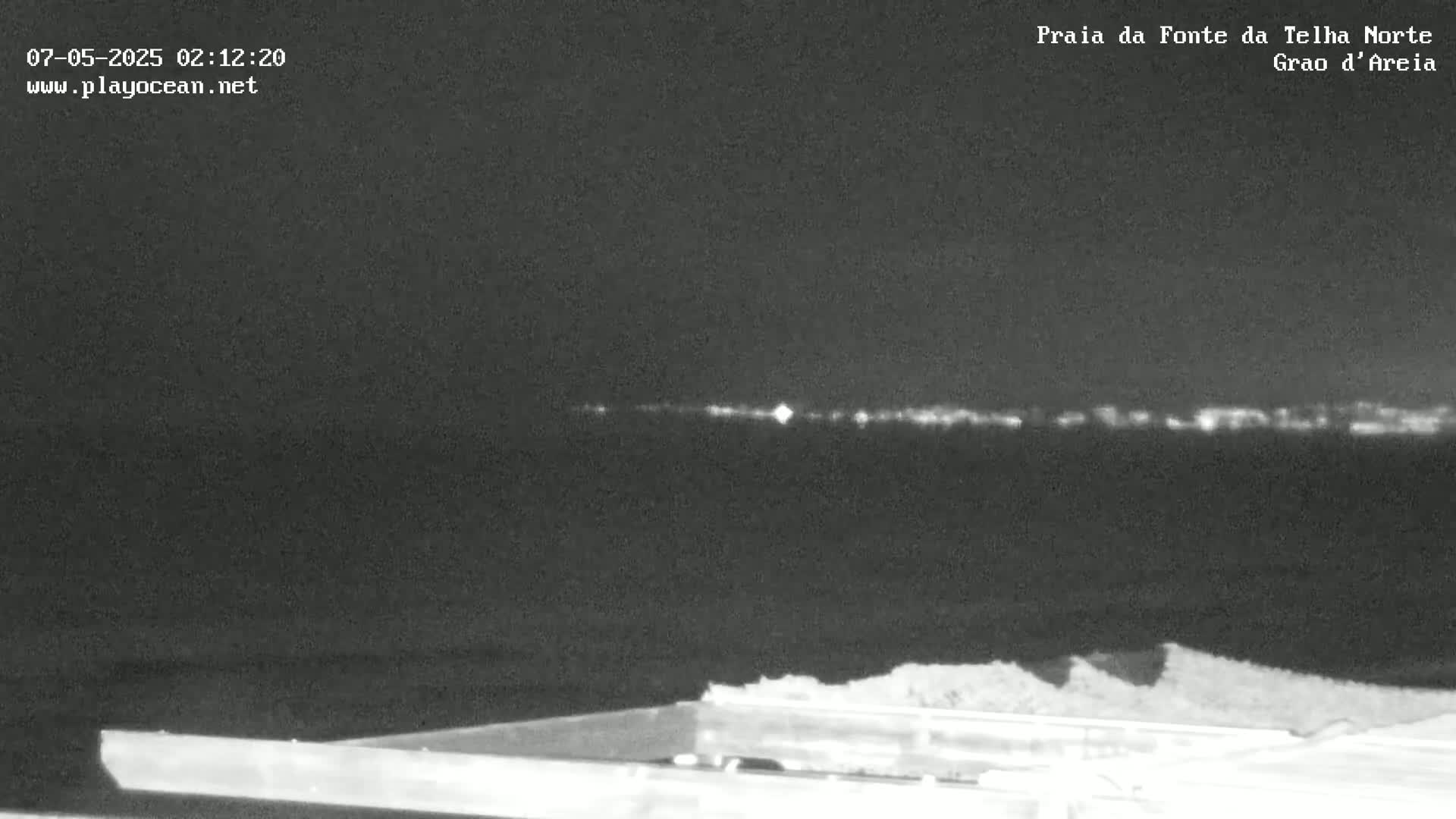 A nighttime, low-light view shows a dark body of water with a distant line of lights on the horizon.
