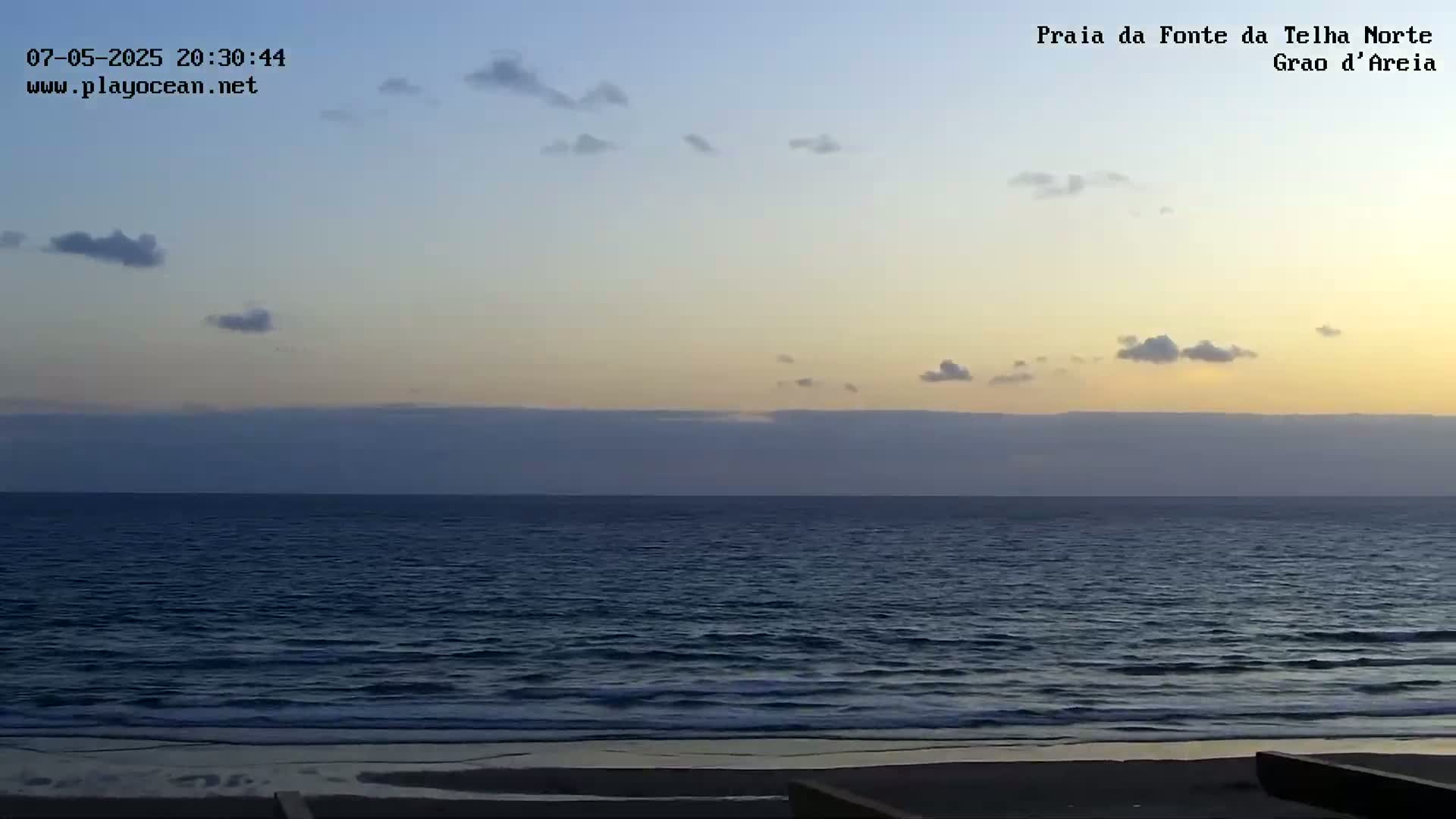 A calm ocean with a few small clouds under a twilight sky meets a sandy beach.