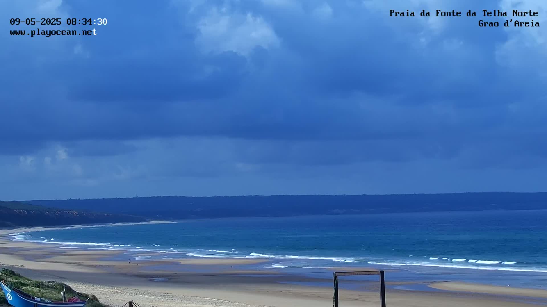A wide sandy beach with gentle waves under a partly cloudy blue sky.
