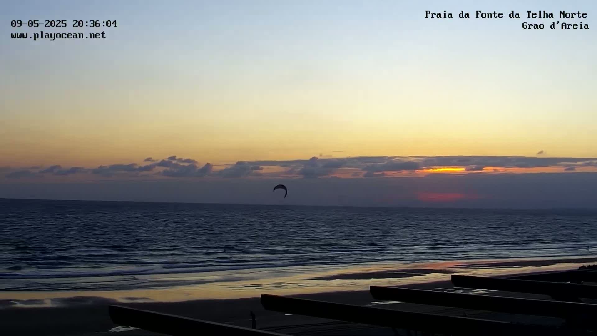 A kitesurfer glides over the ocean at sunset under a partly cloudy sky.