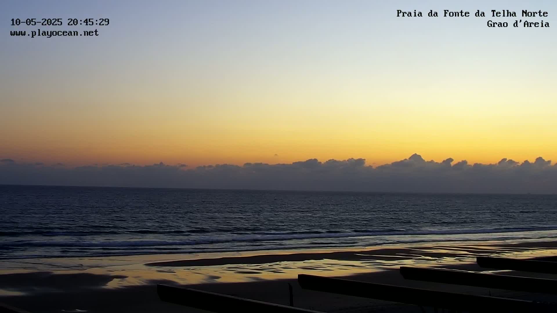 A calm ocean beach at sunset, with a low line of clouds on the horizon.