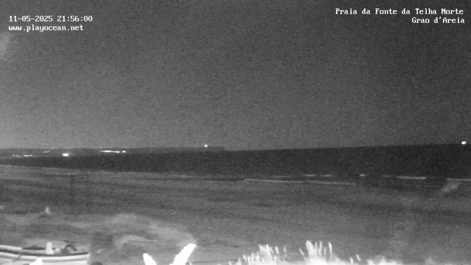 A nighttime, low-light view shows a dark beach and ocean under a clear, dark sky.