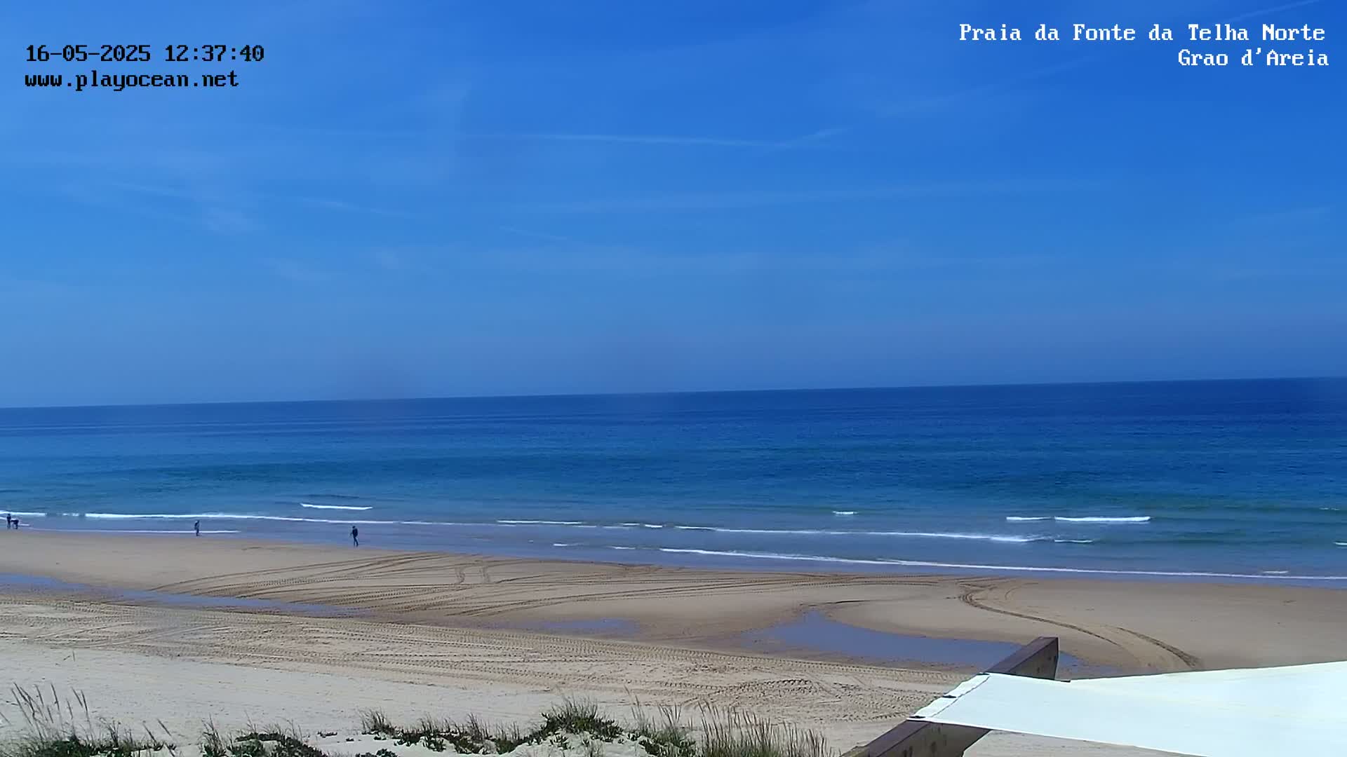 A mostly sunny day shows a wide, sandy beach with tire tracks leading to a calm, blue ocean.
