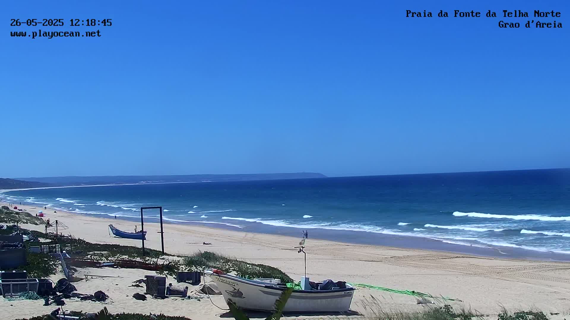 A sandy beach with small waves under a clear blue sky, featuring several small fishing boats pulled ashore.