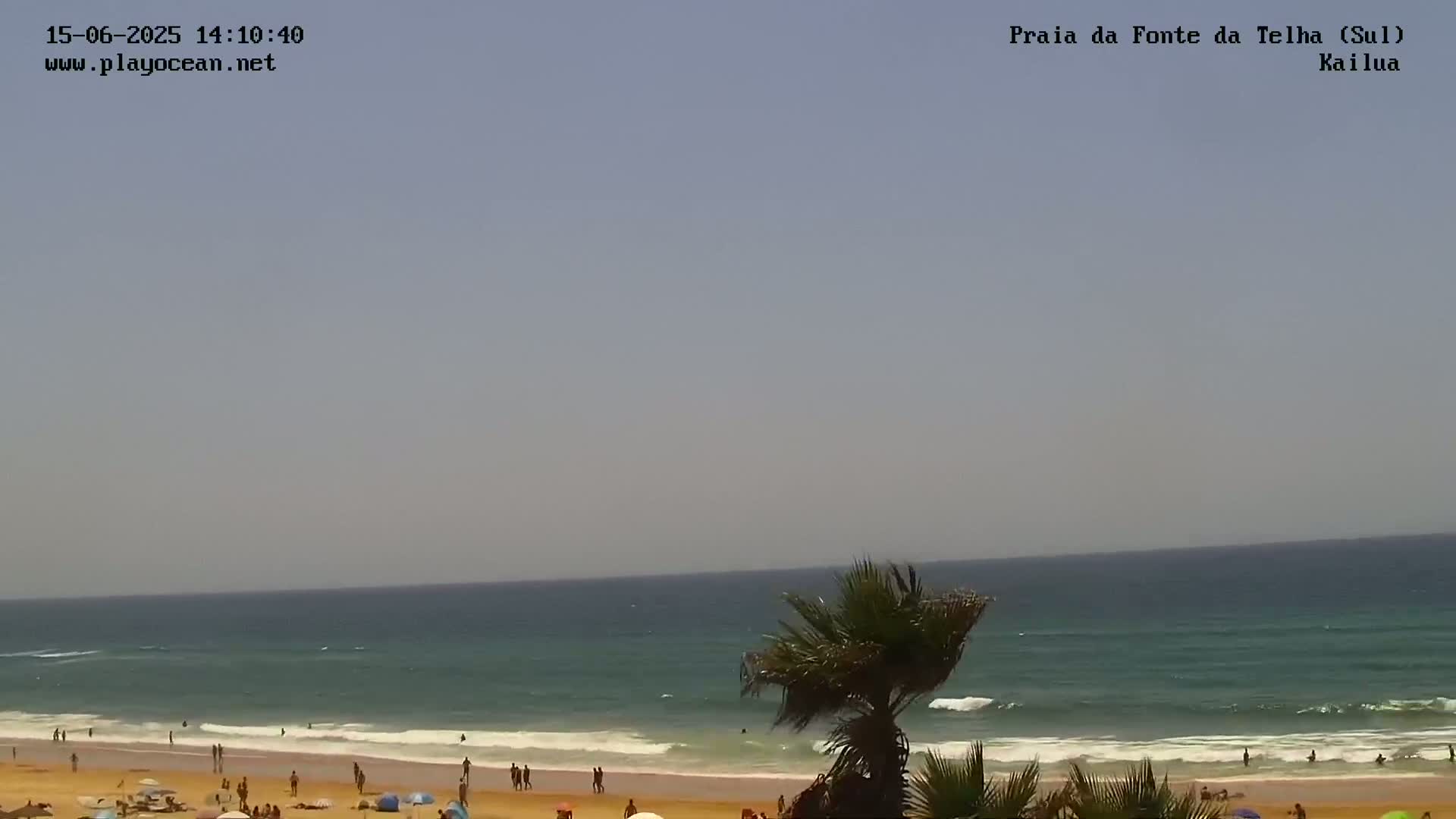 A sandy beach with people and palm trees is visible, with a calm ocean under a hazy sky.