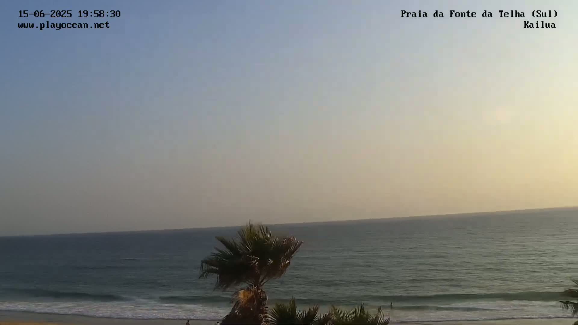 A sandy beach with people and palm trees is visible, with a calm ocean under a hazy sky.