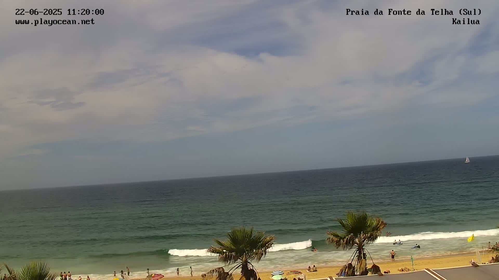 A partly cloudy day at a beach with calm waves, showing people swimming and relaxing on the sand.