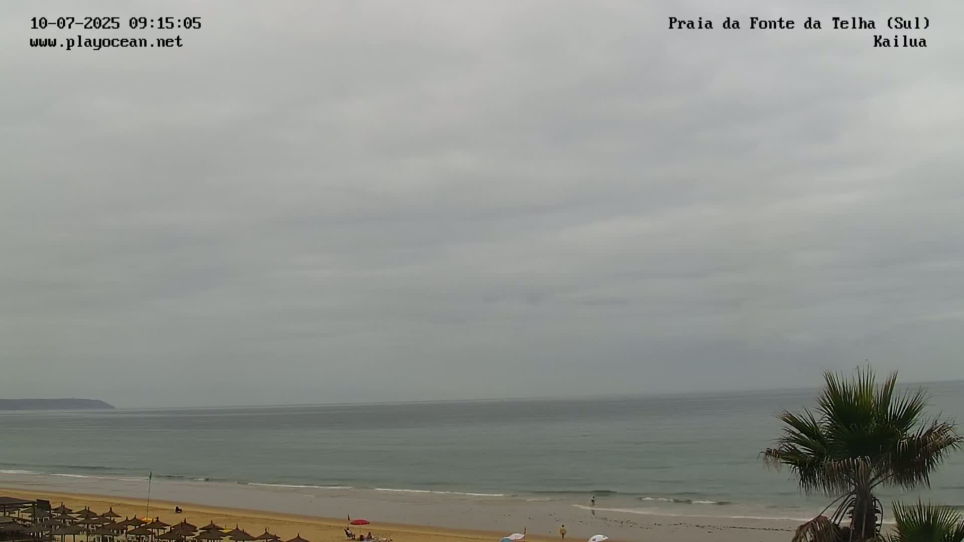 A mostly cloudy sky overlooks a calm ocean and sandy beach with a few people and umbrellas.