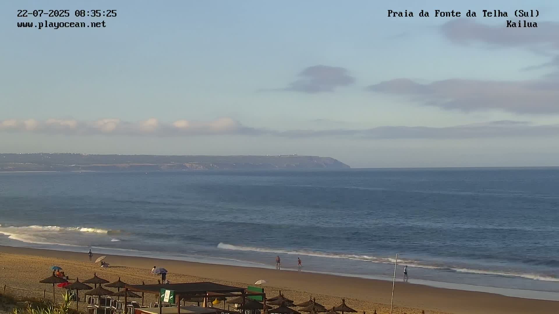 A sandy beach with calm ocean waves and a few people is visible under a mostly clear sky with some scattered clouds.
