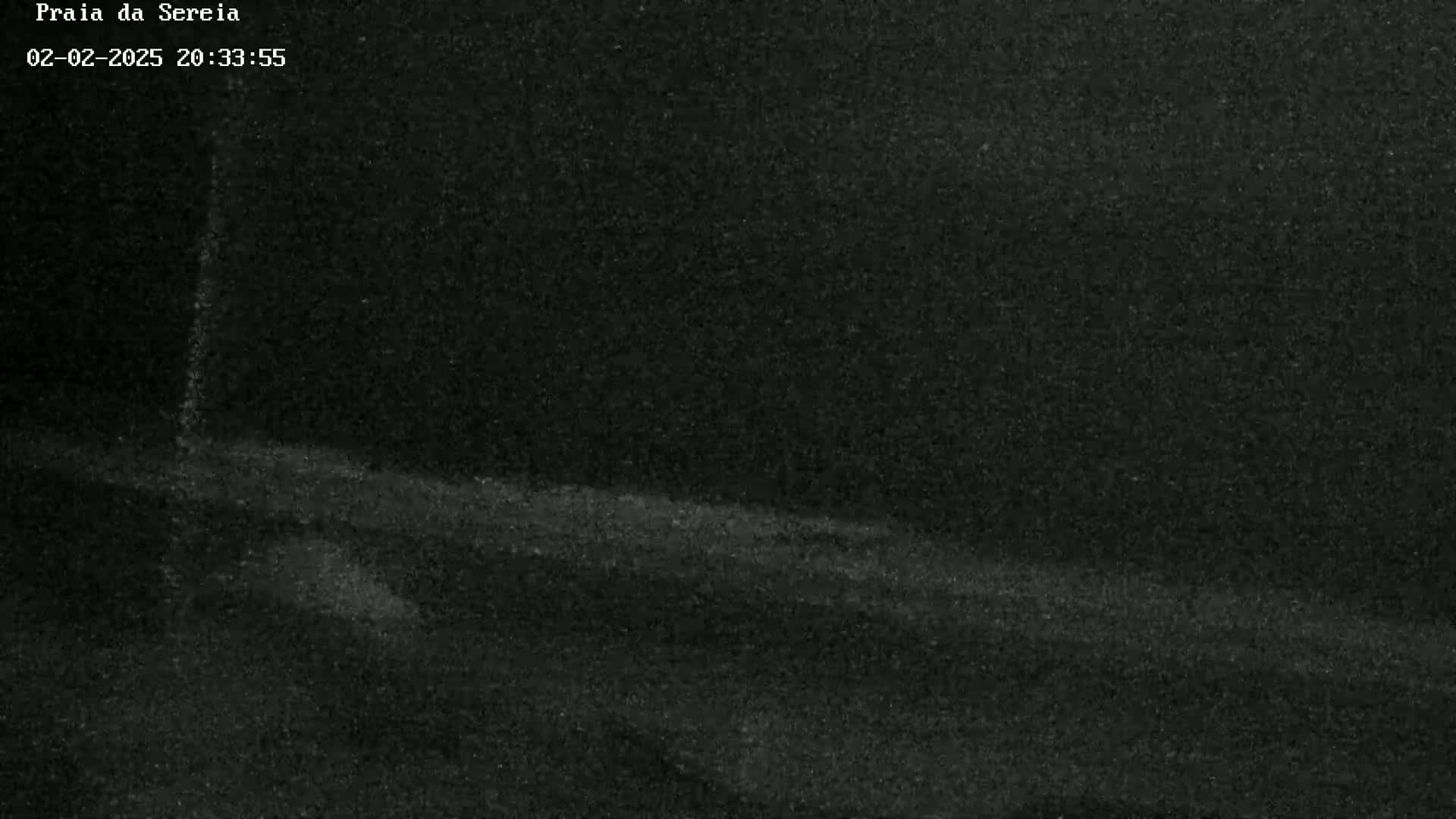 A low-light nighttime image shows a dark, possibly sandy, ground sloping gently upward.