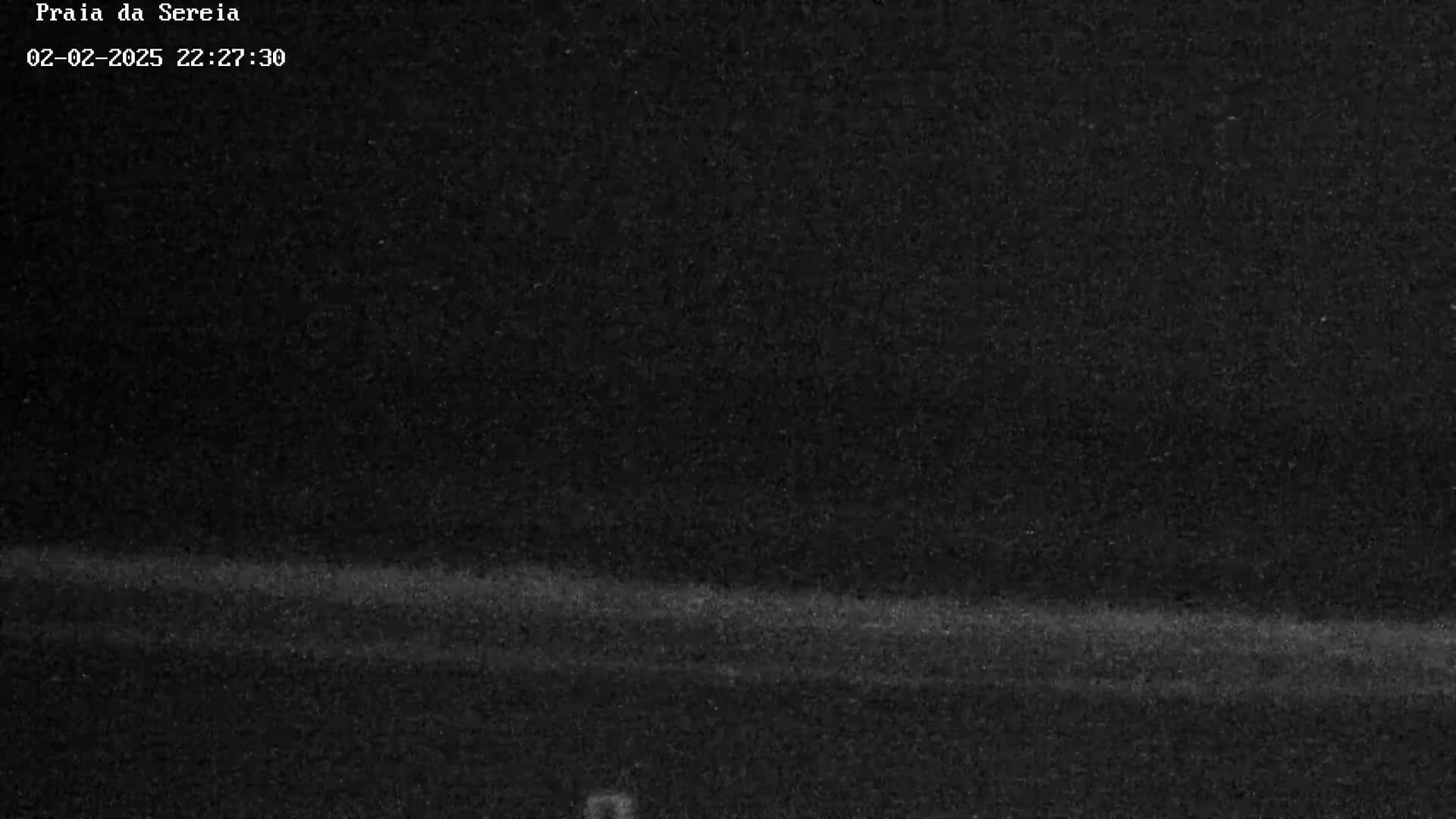 A low-light, nighttime image shows a dark, flat expanse of land, possibly a beach or field, under a dark sky.