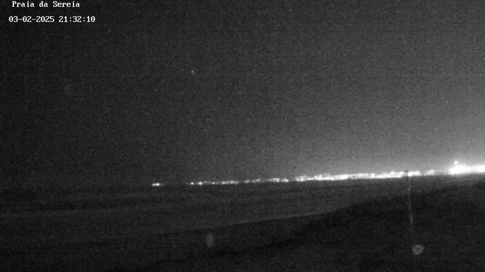 A nighttime, low-light view shows a distant line of lights on the horizon.