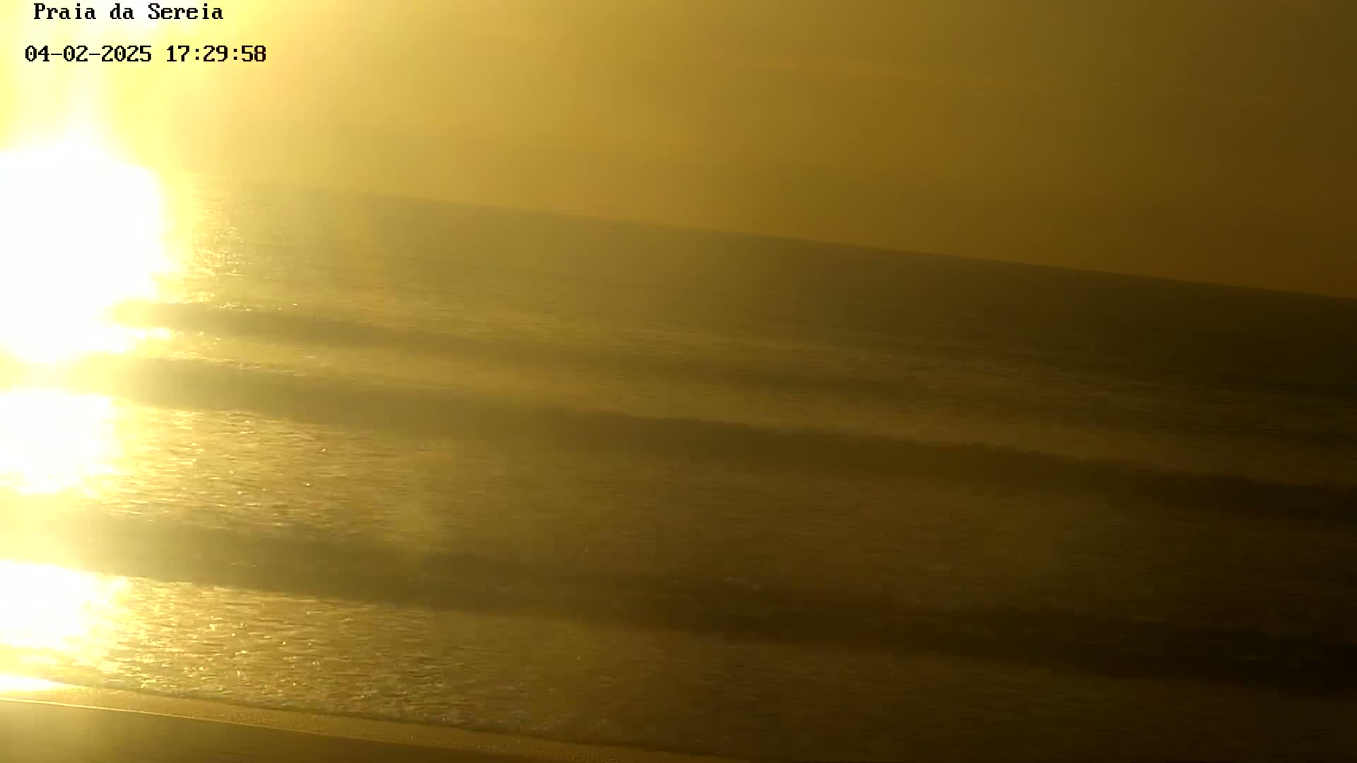 A hazy, golden sunrise casts its light over gentle ocean waves.