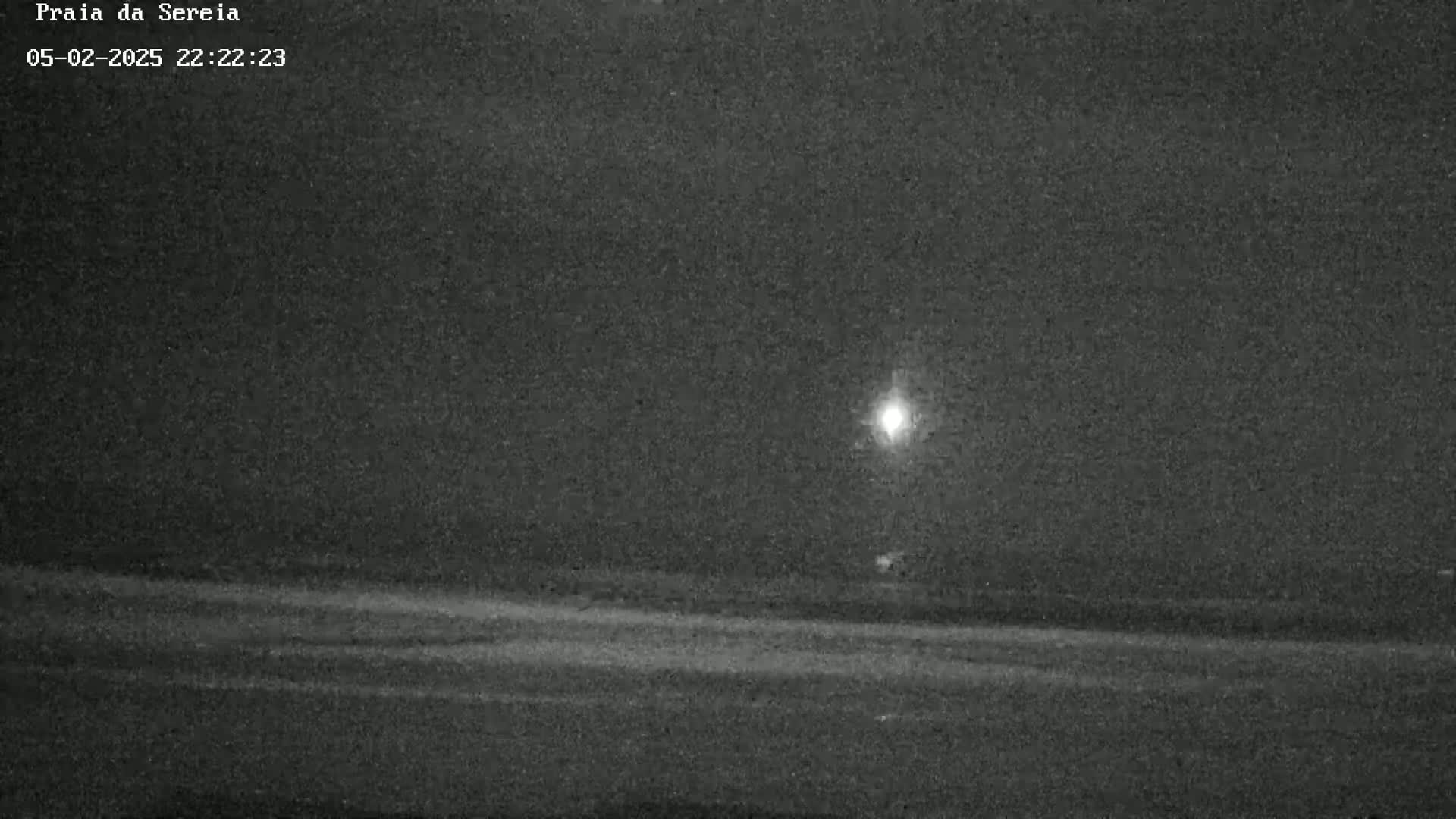 A nighttime, low-light image shows a flat, dark landscape with a single bright light source in the distance.