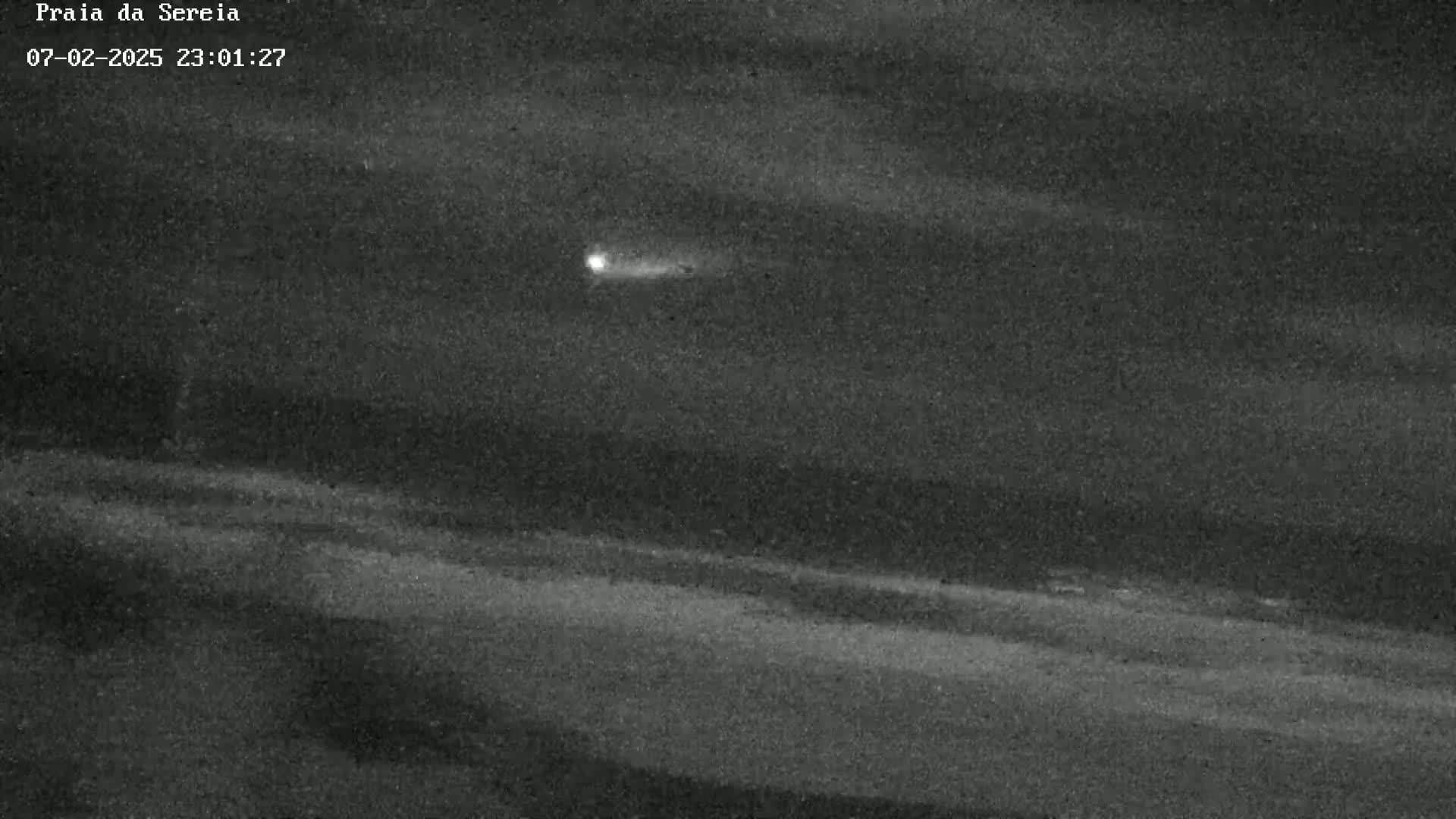 A bright streak of light moves across a dark, night sky above a flat, dark landscape.