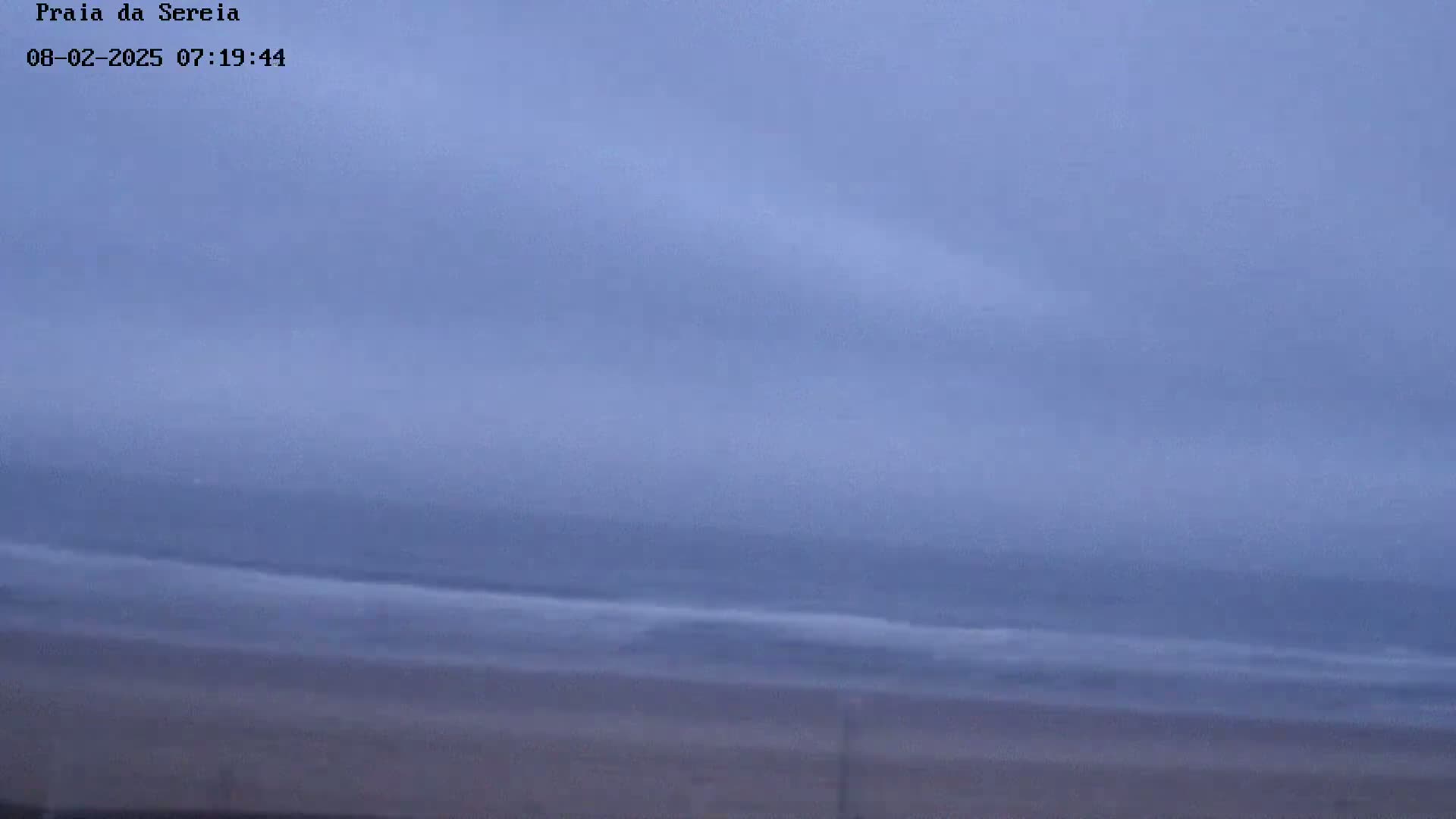 A beach is shown under an overcast sky with a calm ocean.