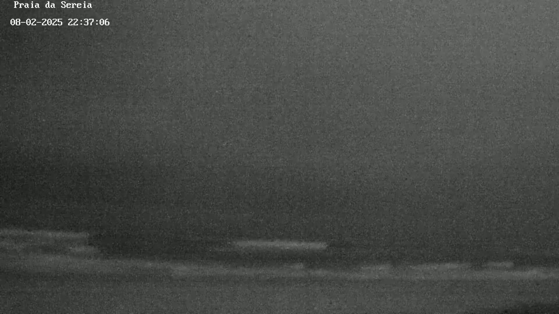 A dark, grainy nighttime image shows a dark horizon line separating a dark sky from an equally dark body of water.