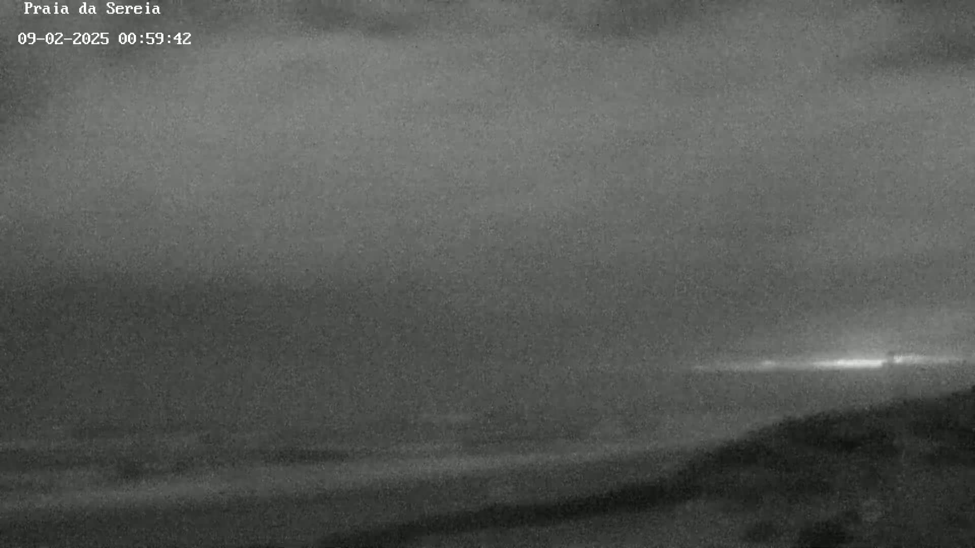 A nighttime, low-light view of a dark beach and ocean under an overcast sky.
