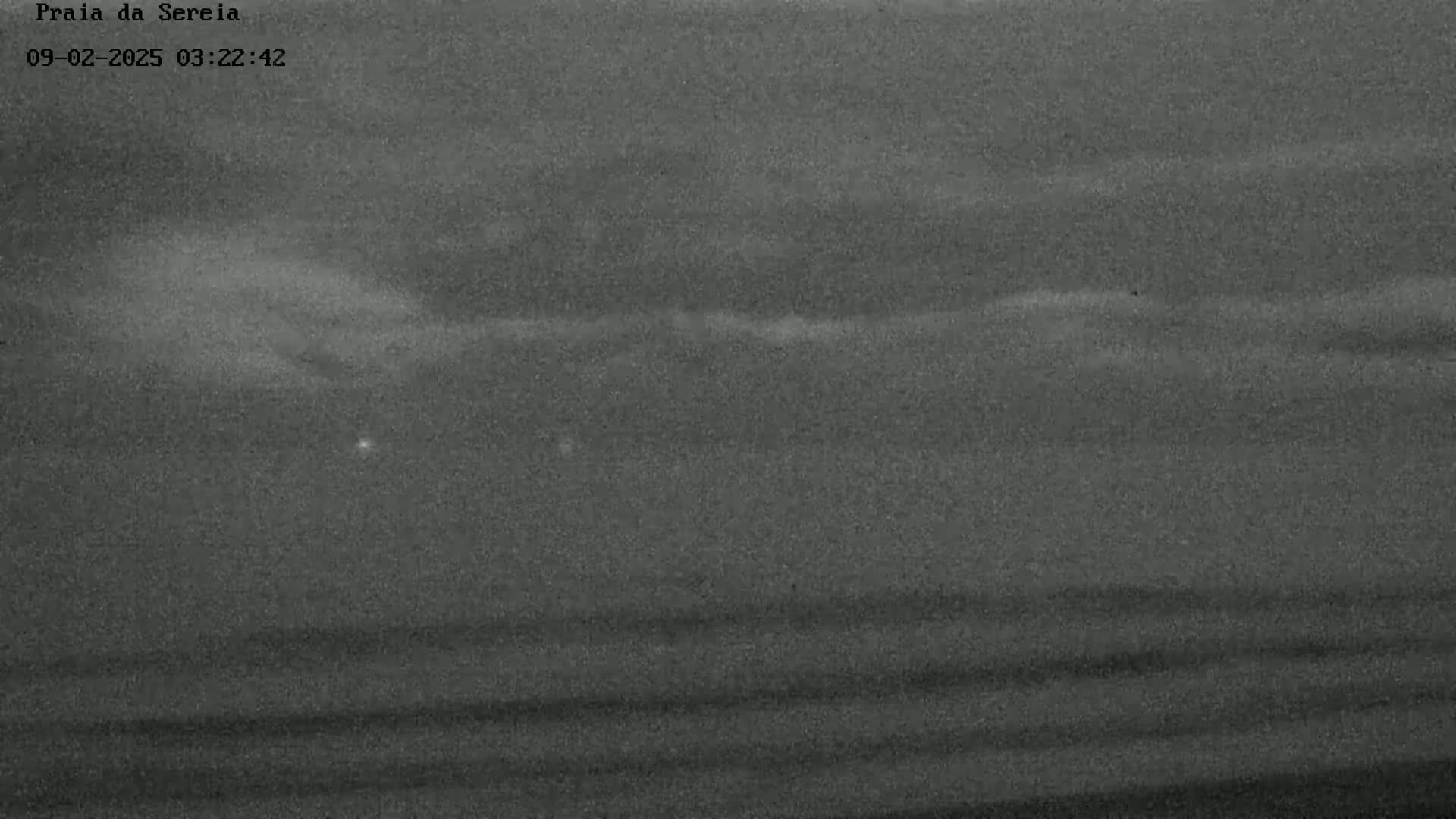 A low-light nighttime image shows a dark, cloudy sky over a beach.