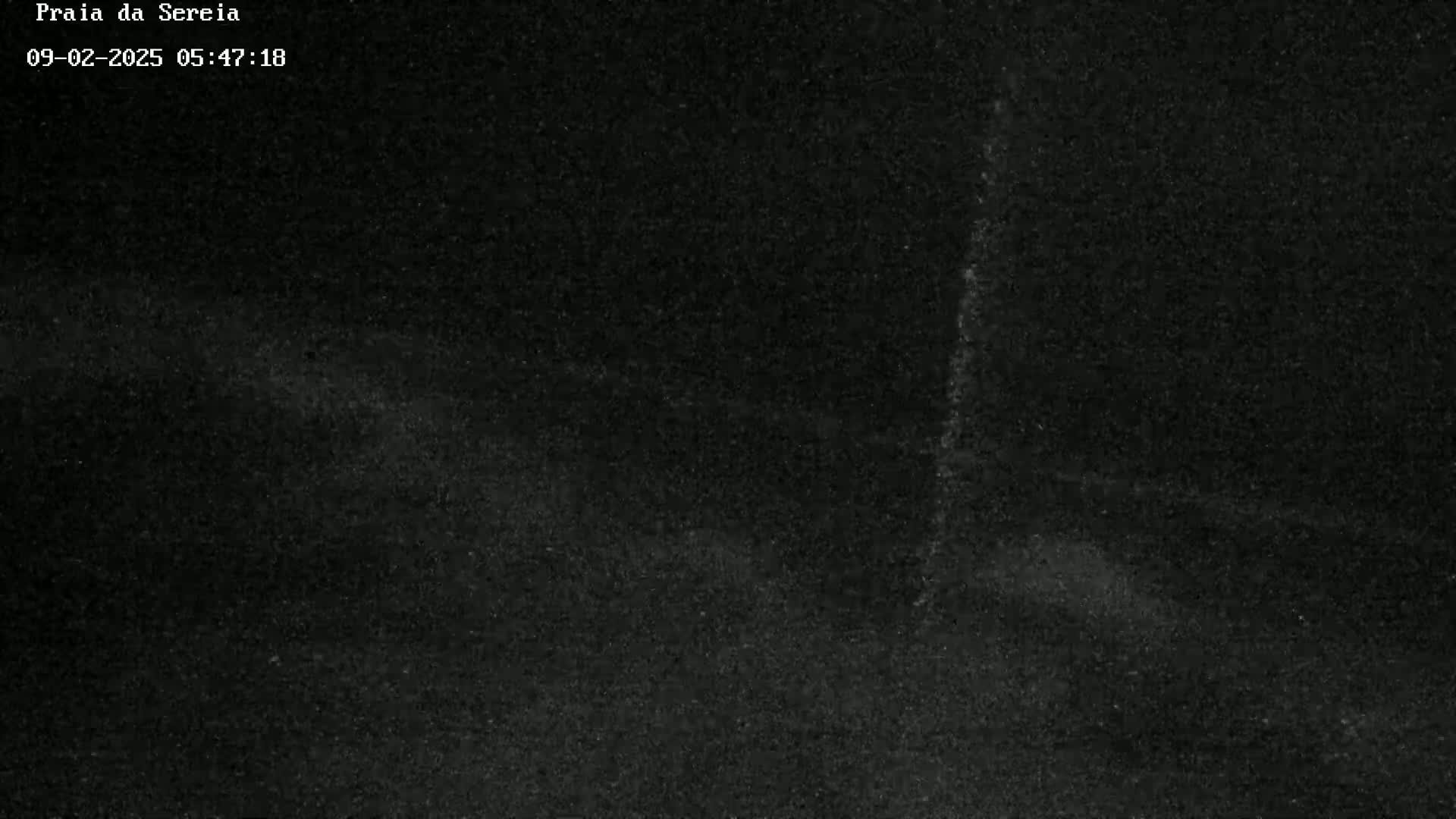 A dark, grainy image shows a mostly black scene with a faint vertical streak of lighter gray.