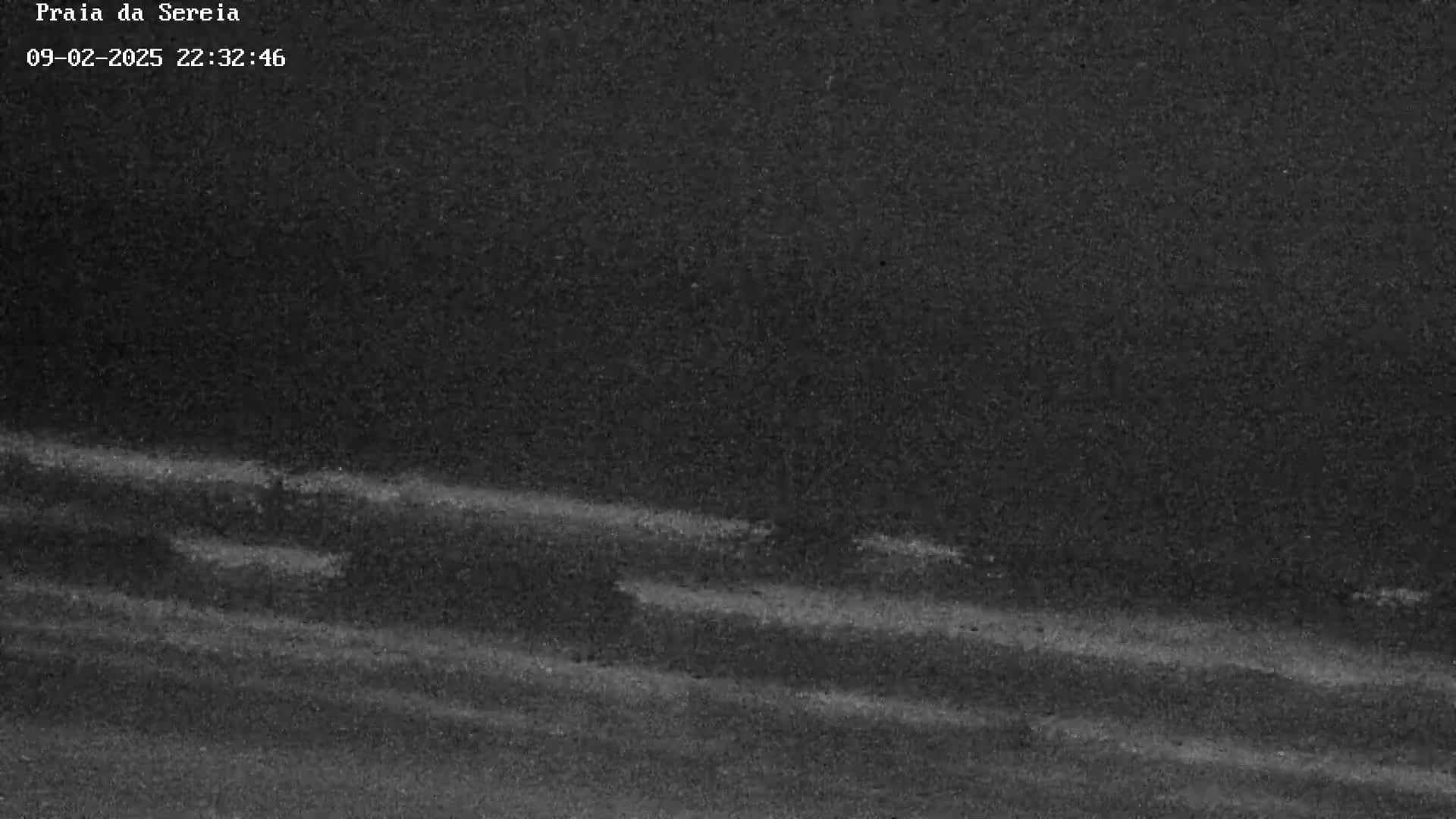 A dark, grainy image shows faint, horizontal streaks of lighter gray against a mostly black background, possibly suggesting a nighttime beach scene with low light conditions.