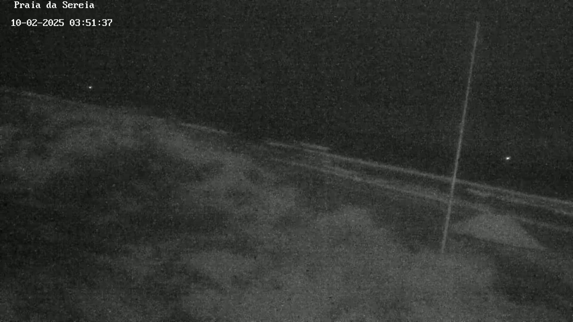 A nighttime, low-light image shows a dark, flat expanse of land with a faint, light-colored line running diagonally across it, intersected by a vertical line.