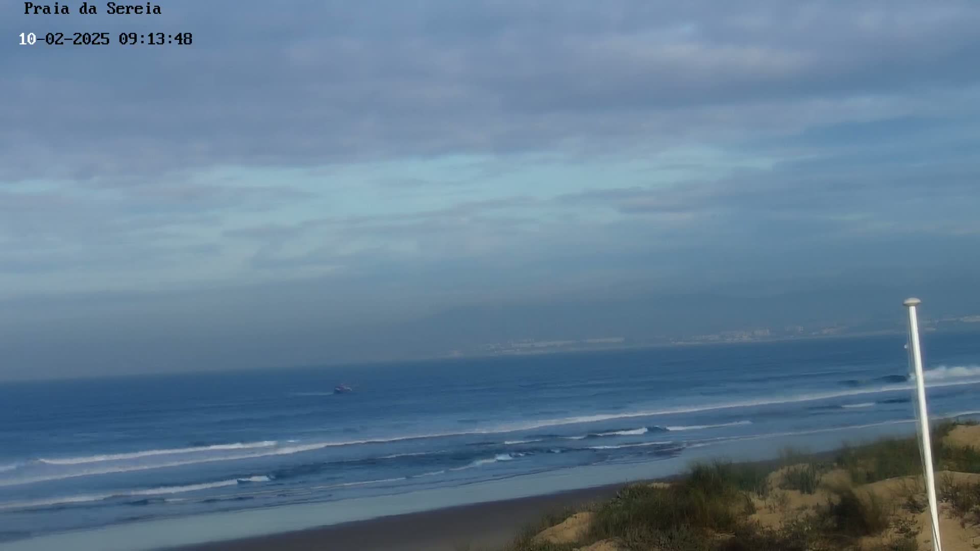A mostly cloudy sky overlooks a beach with gentle waves rolling onto the shore.