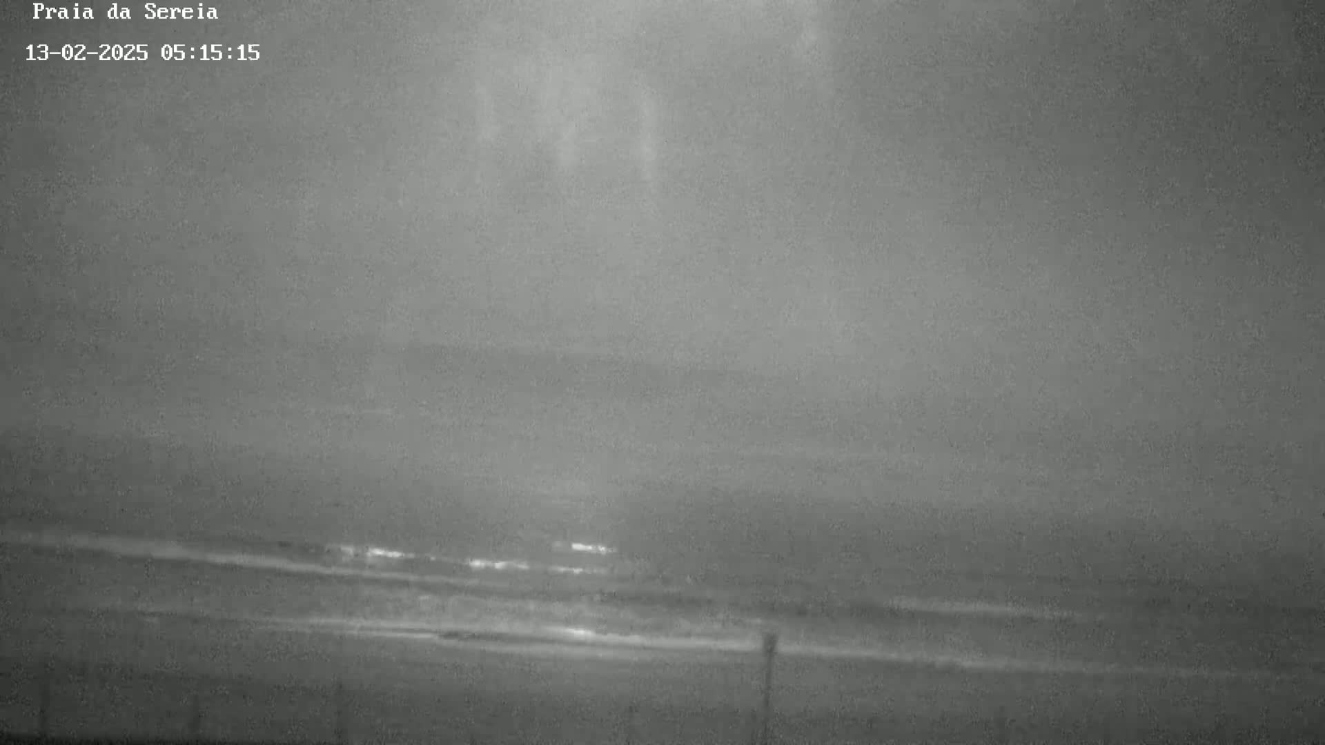 A dark, overcast night scene shows a beach with gently rolling waves.
