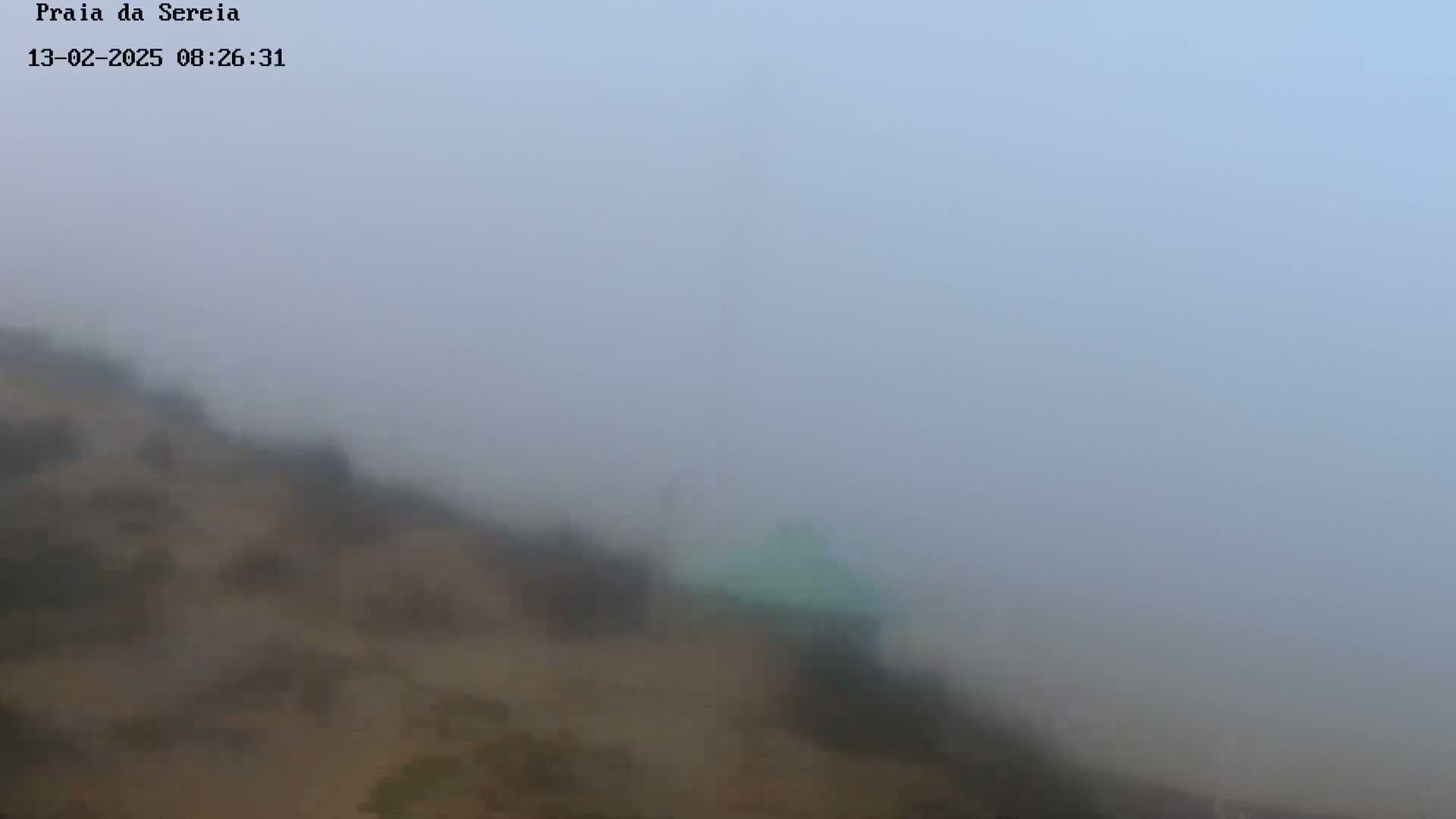 A hazy, foggy scene shows a tan hillside and a hint of a light green structure in the midground.