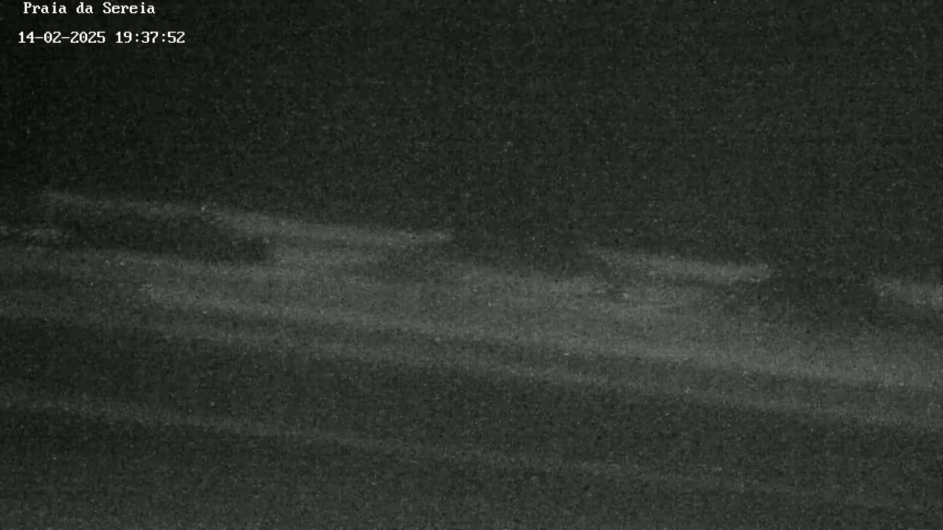 A dark, grainy image shows a dimly lit, possibly sandy, expanse under a nighttime sky.