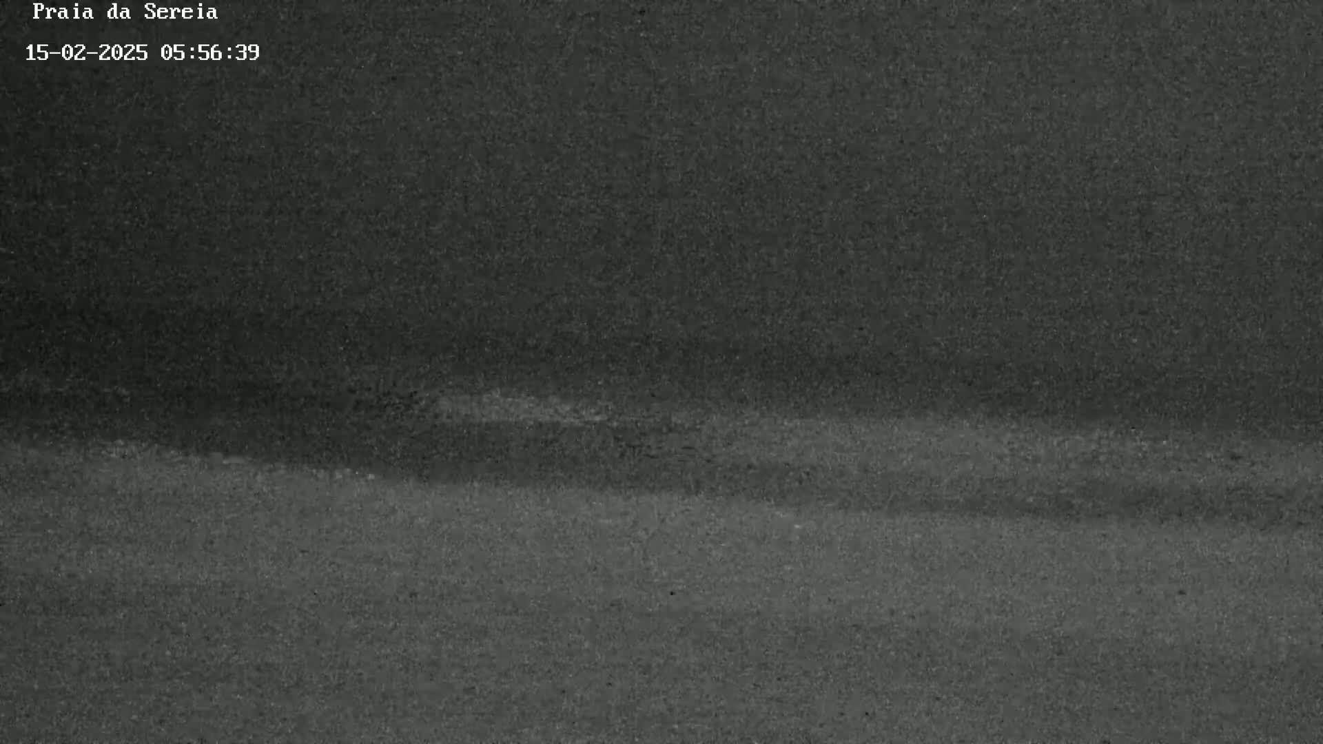 A dark, possibly nighttime, outdoor scene shows a mostly flat expanse of dark sand or beach.