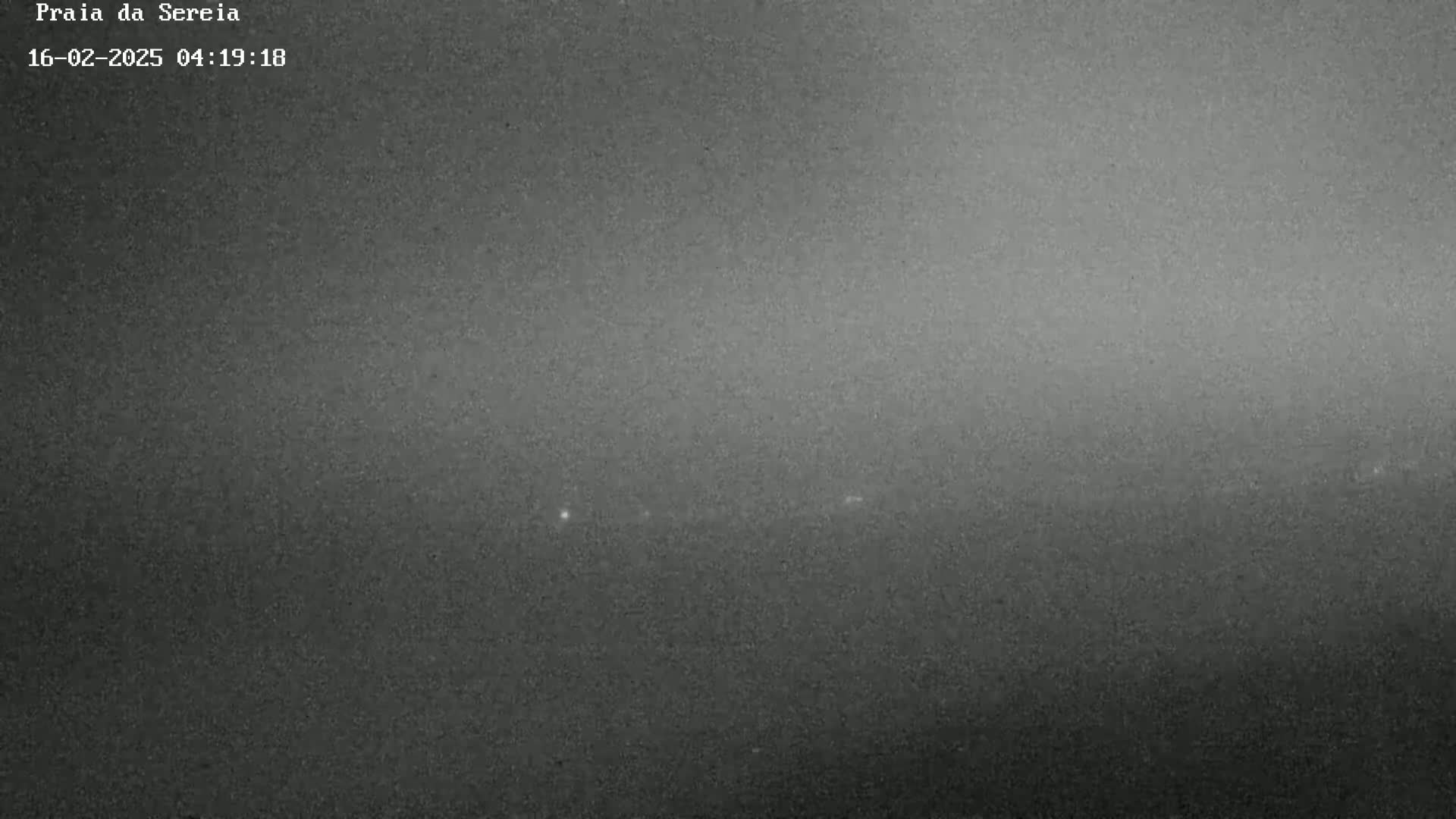 A grainy, dark gray image shows a nighttime outdoor scene with a faint horizontal line of lights in the center.