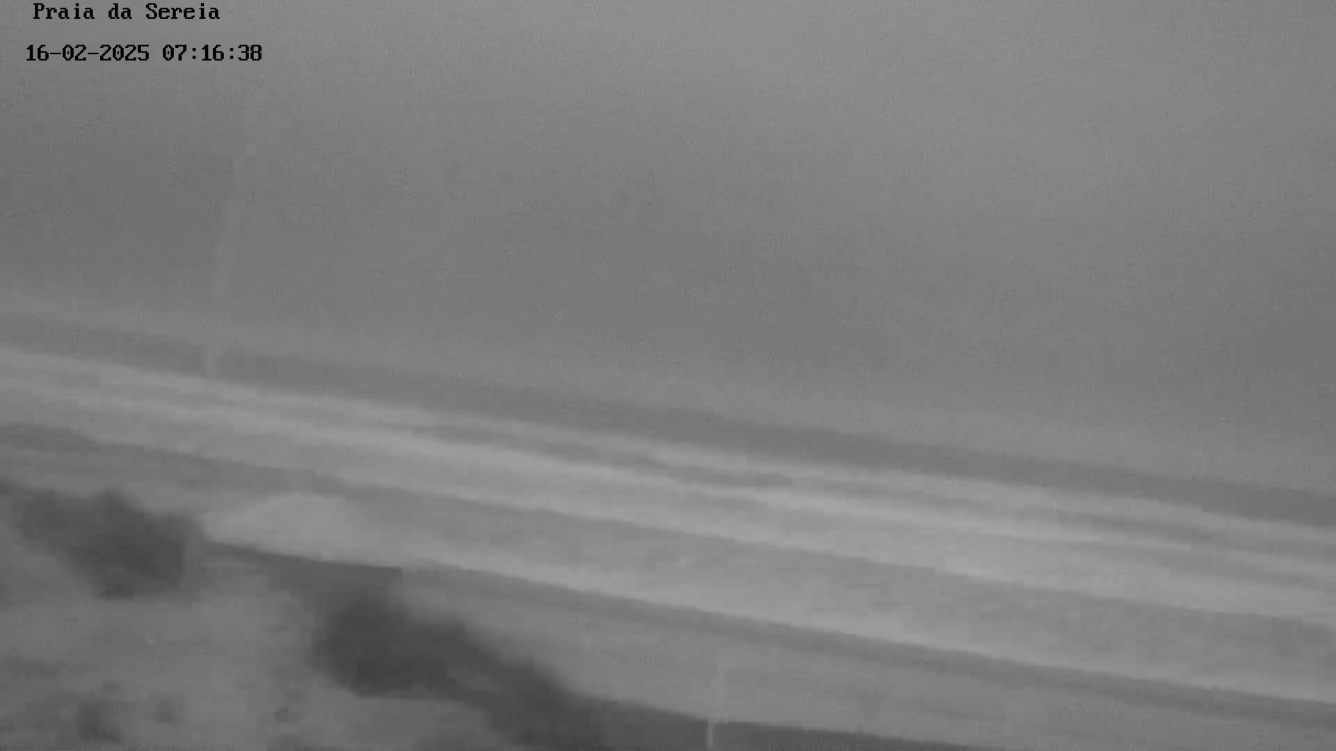 A hazy, overcast day shows a beach with faint waves and some indistinct land features in the foreground.