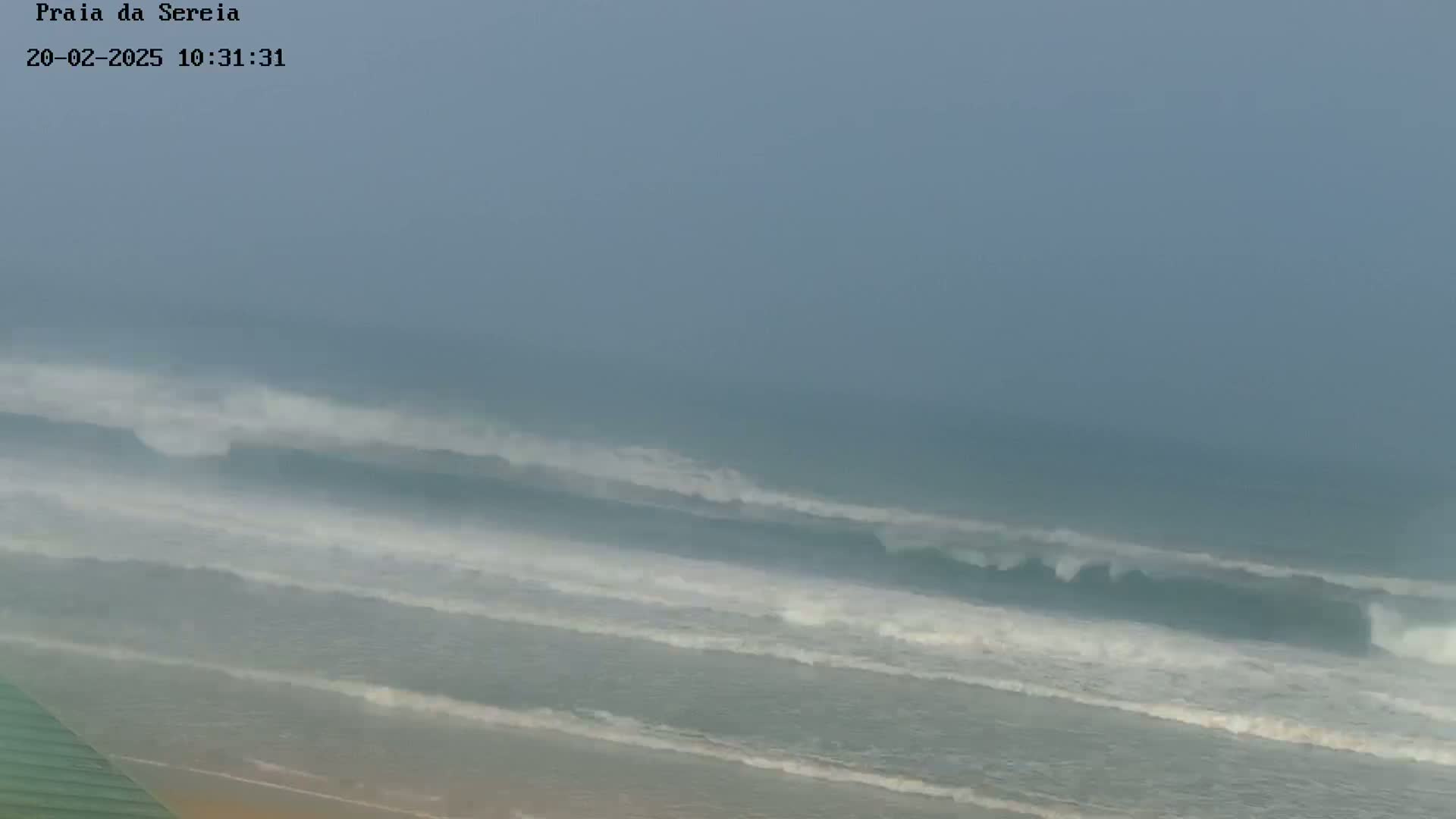 Large waves crash on a beach under an overcast sky.