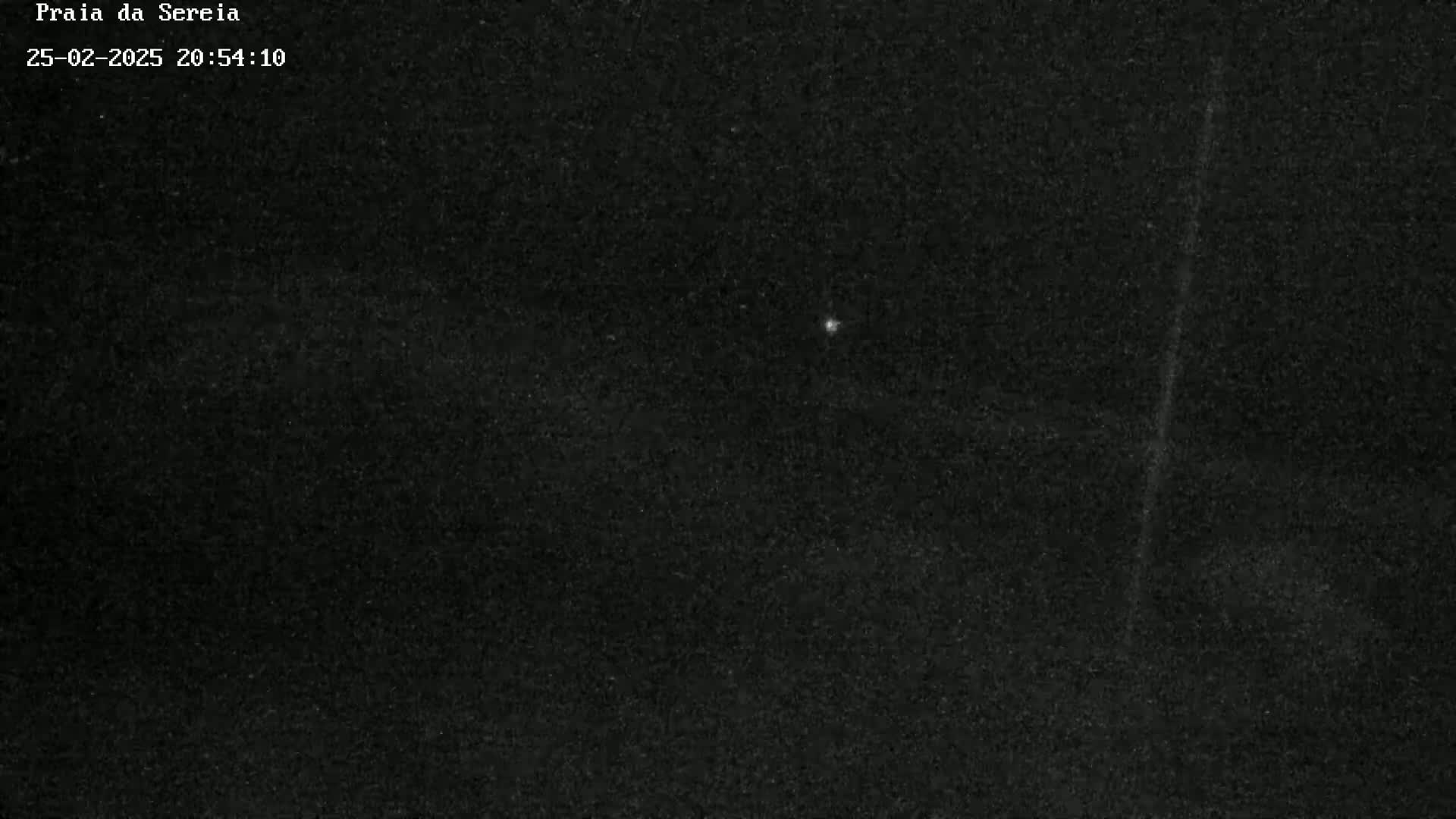 A nighttime outdoor image shows a dark sky with a single, faint light source and a vertical streak.