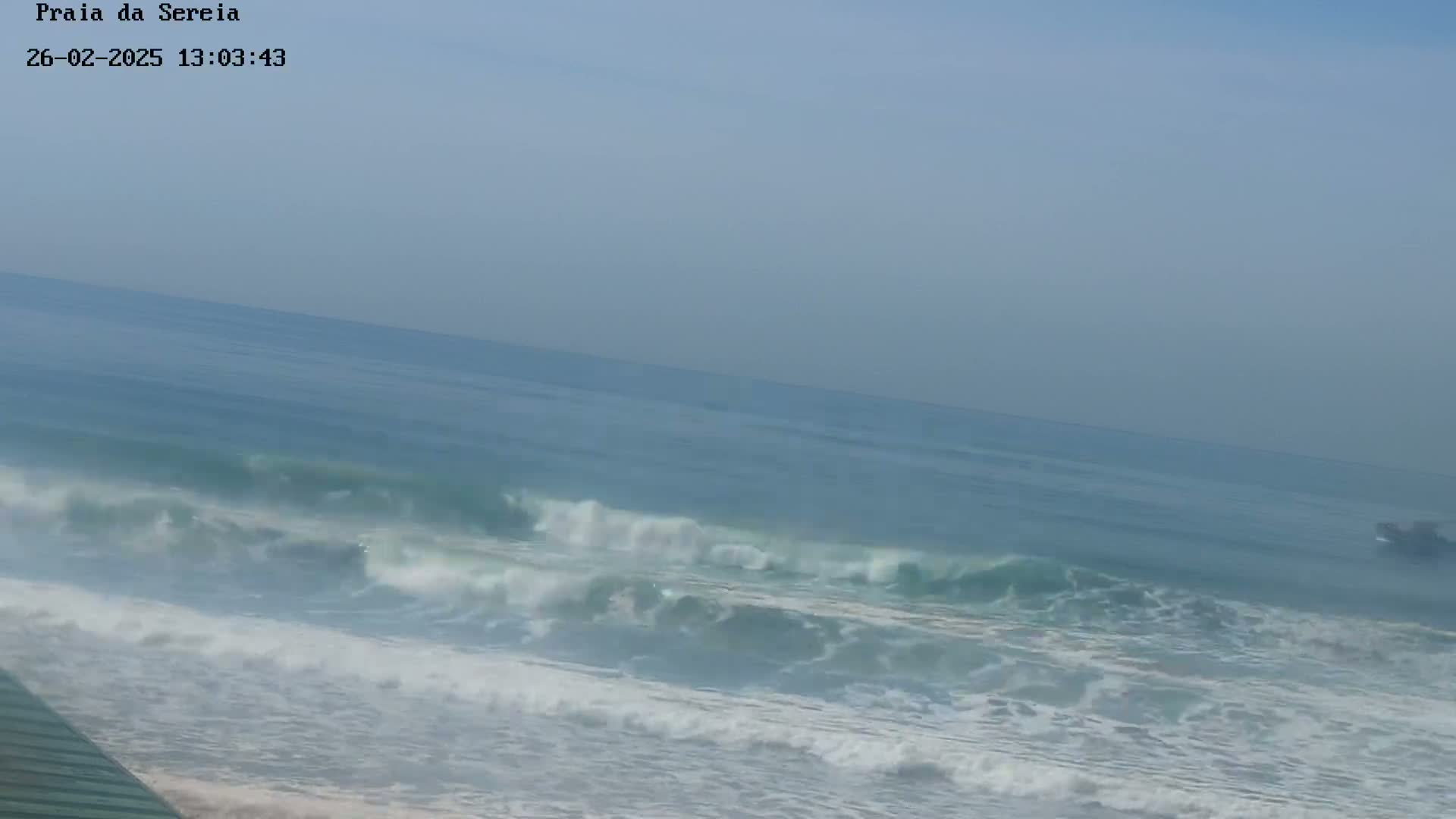 A hazy, somewhat overcast day shows moderate waves breaking on a beach.