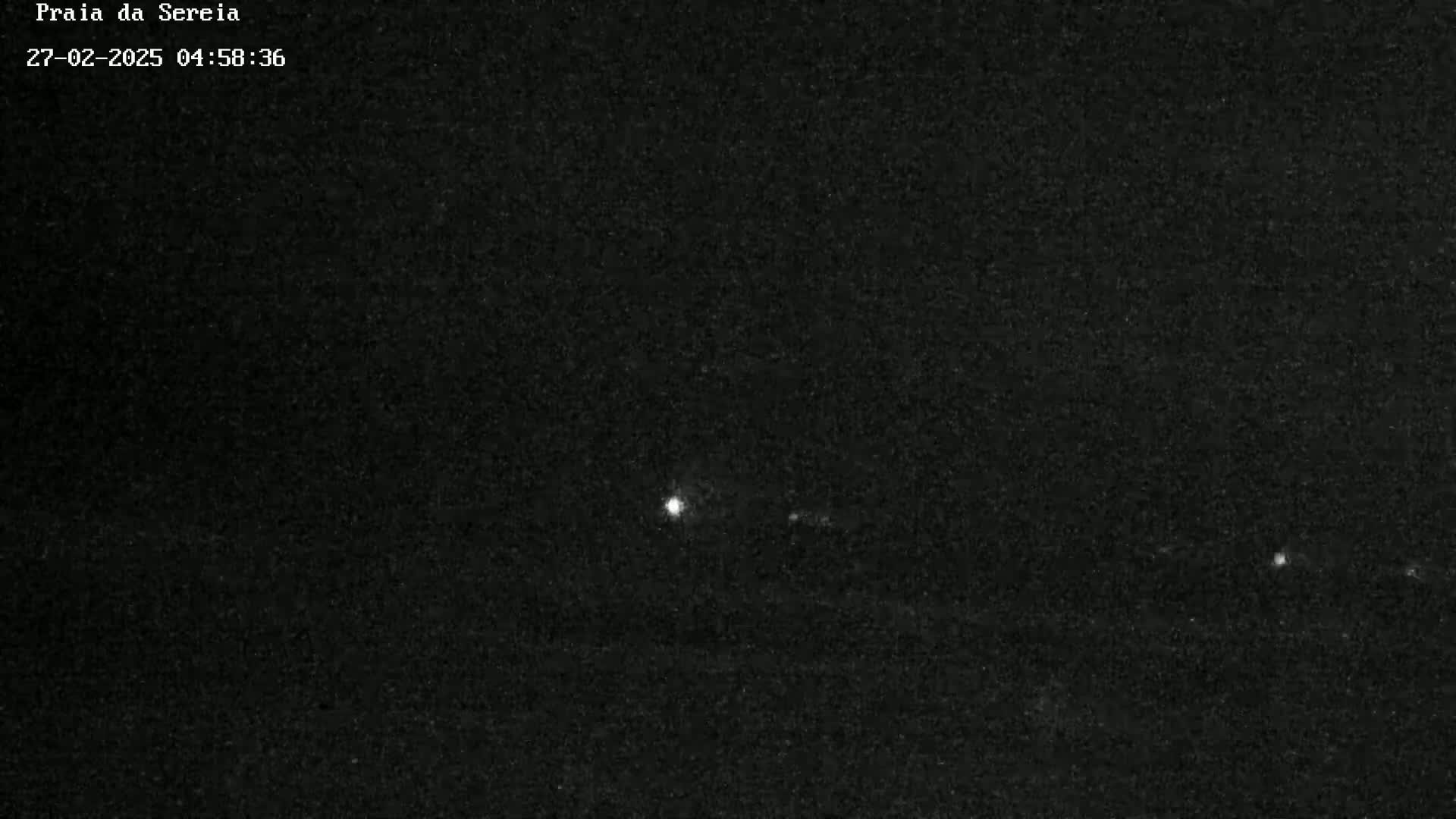 A nighttime image shows a few distant, bright lights in a dark, grainy scene.