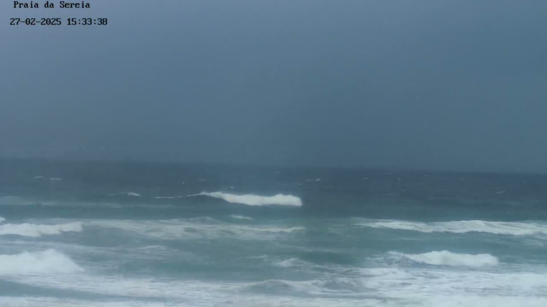 A grey, overcast sky hangs over a choppy ocean with moderate waves breaking near the shore.