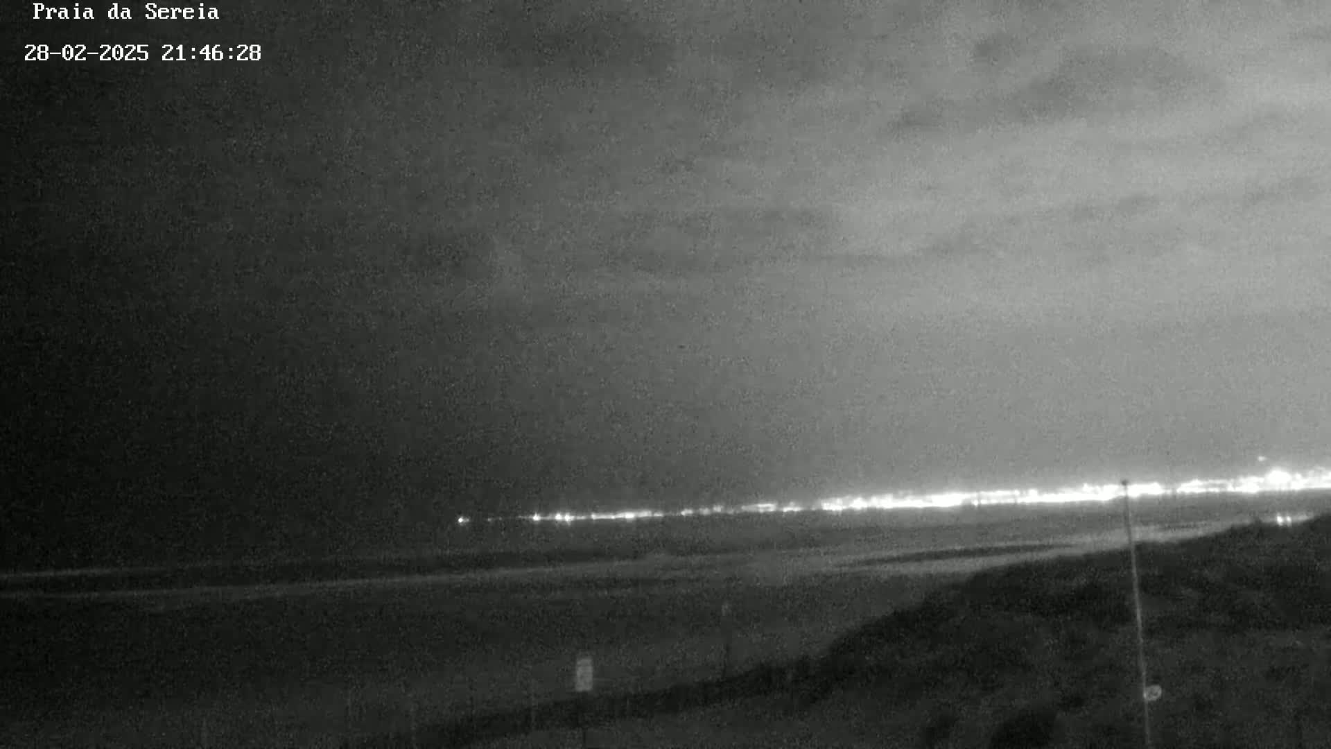 A nighttime, overcast view of a beach with a distant line of lights visible on the horizon.