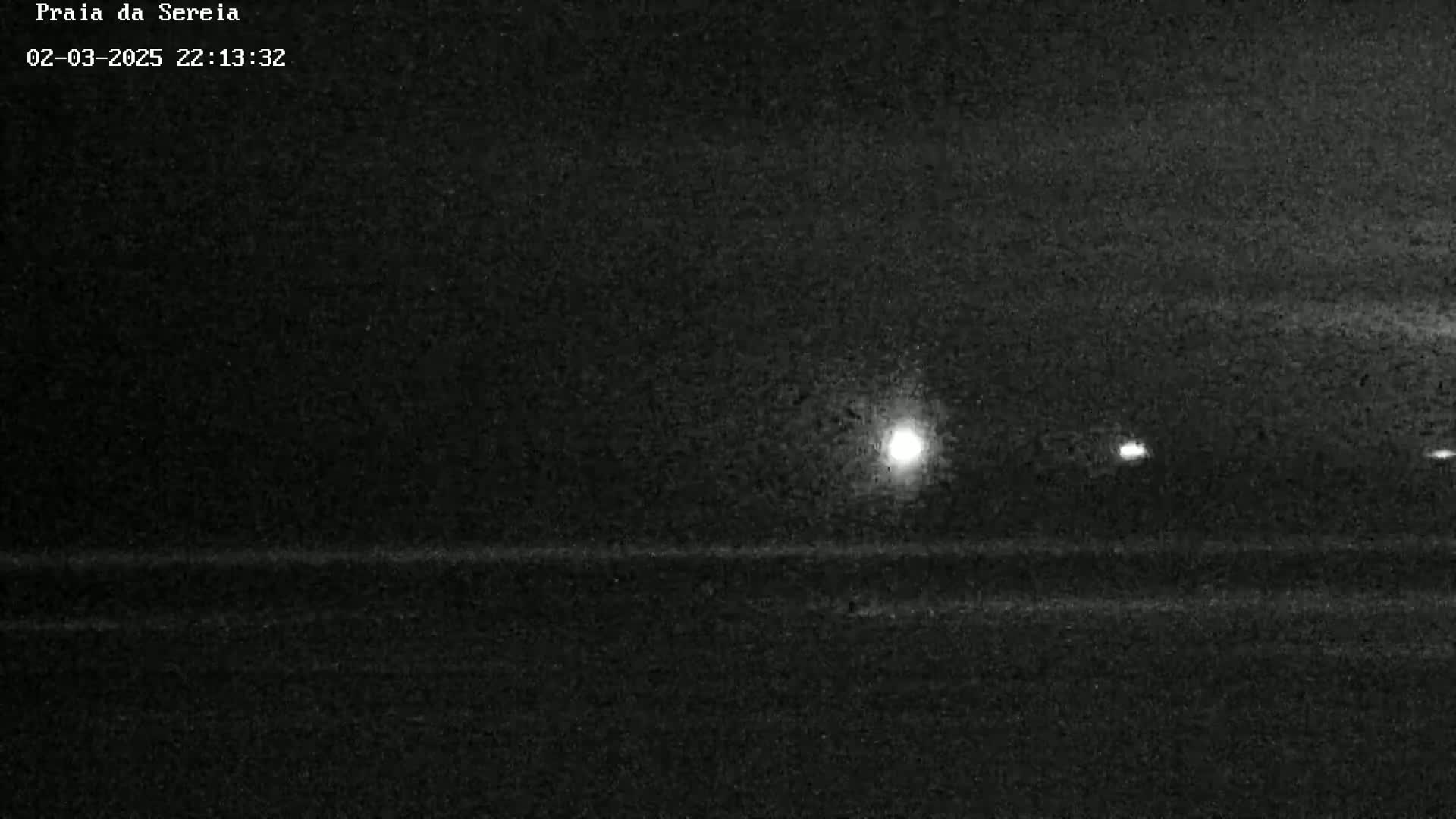 A nighttime, low-light image shows a dark, flat landscape with a few distant lights visible.