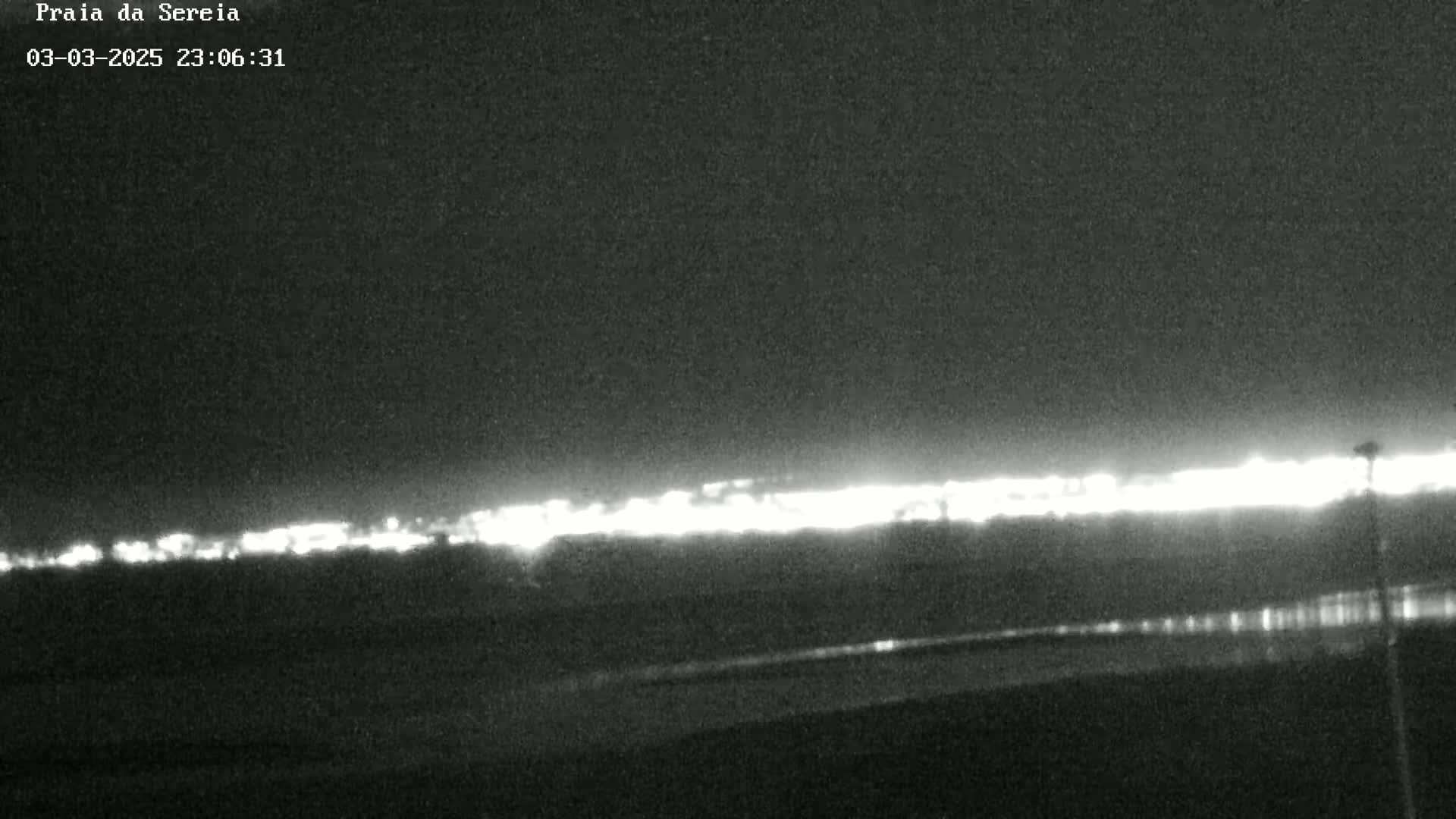 A nighttime, low-light image shows a distant line of lights on the horizon under a dark, clear sky.