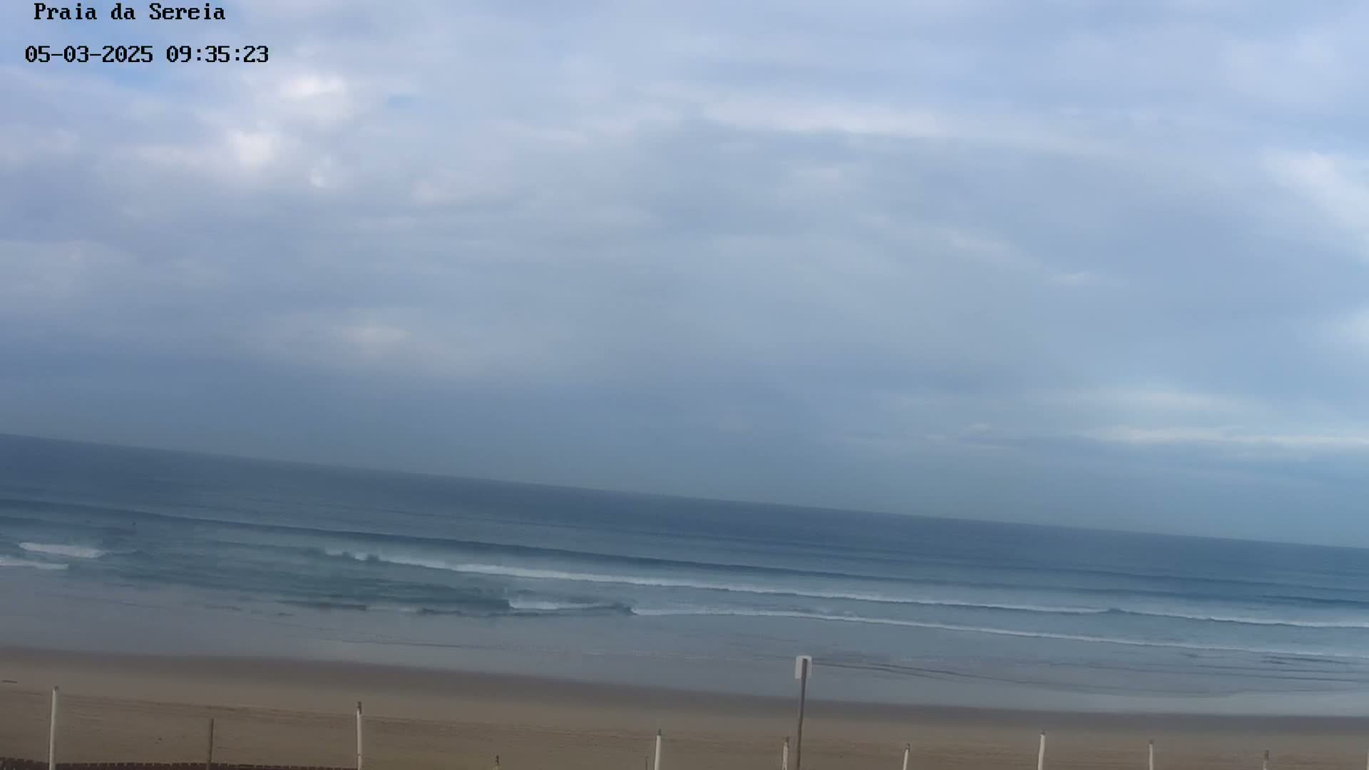 An overcast sky hangs over a beach with gently rolling waves.