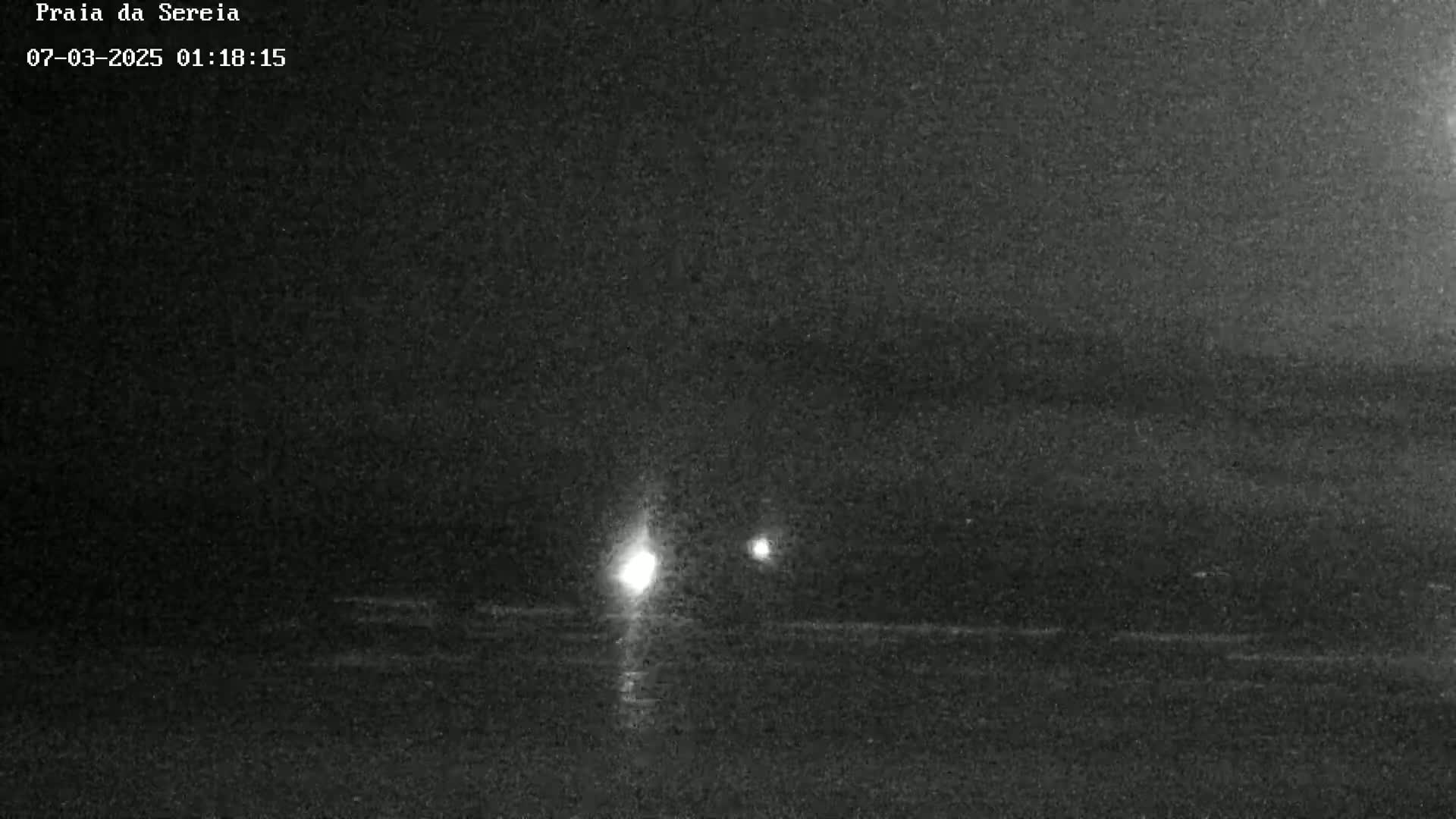At night, two distant lights are visible over dark water.