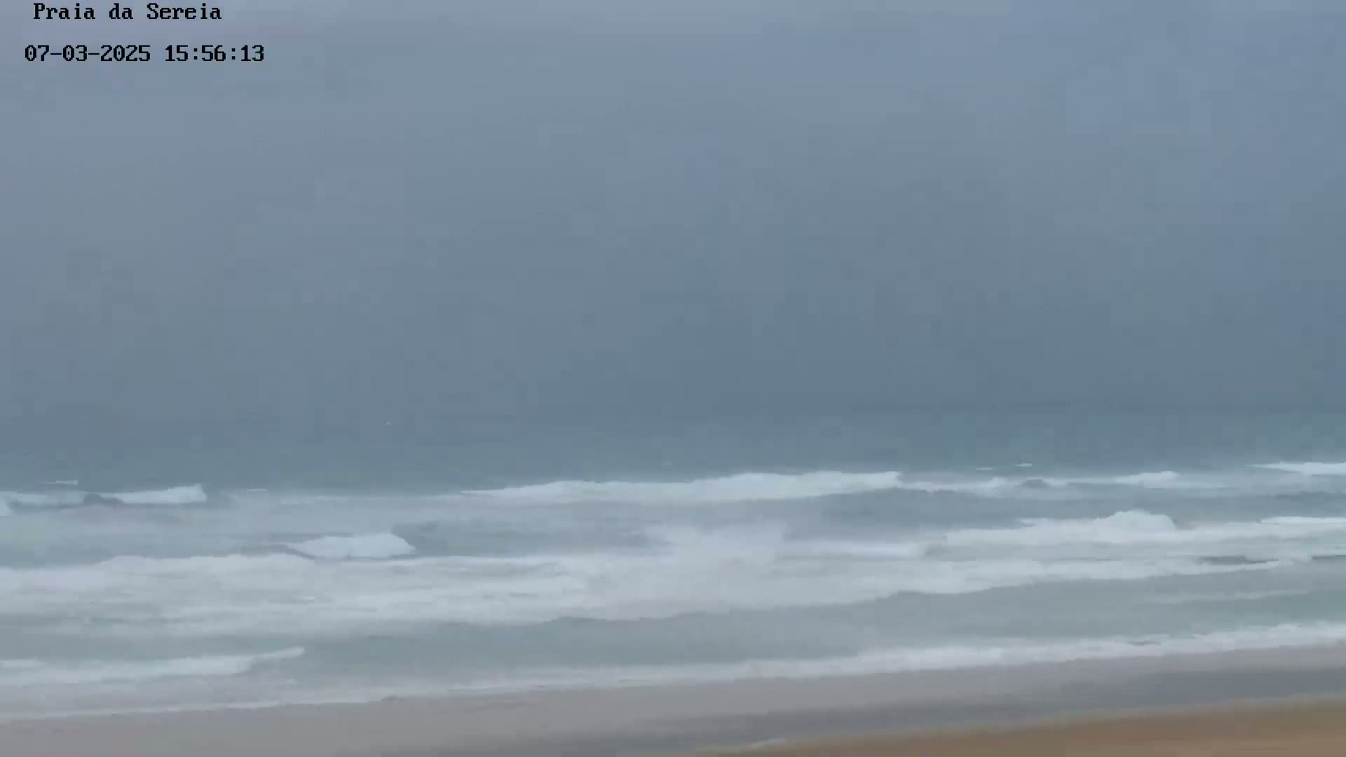 A beach with moderate waves is visible under an overcast sky.