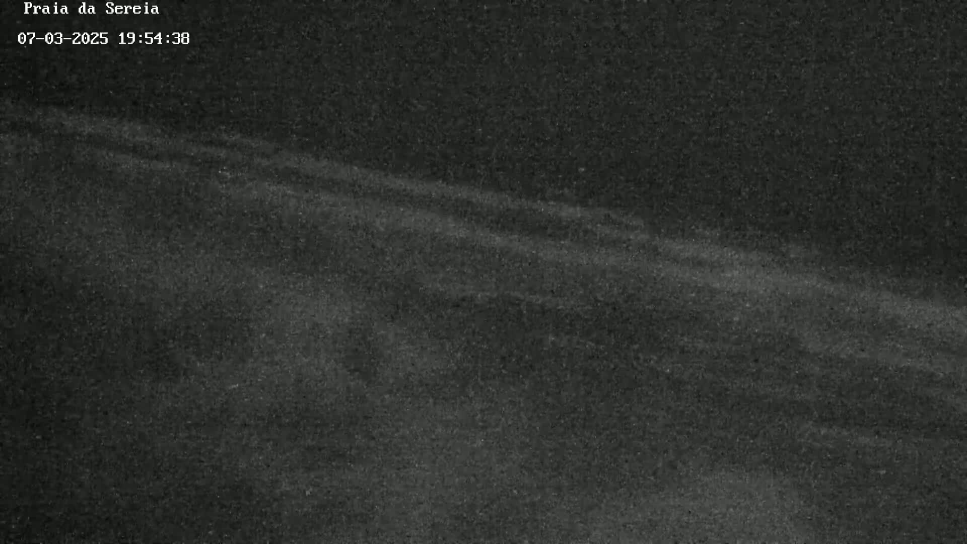 A dark, grainy image shows a dimly lit, possibly nighttime scene with faint streaks of light across a textured surface.