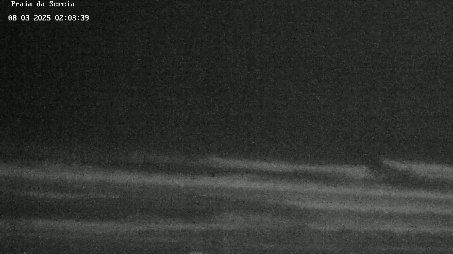 A dark, nighttime outdoor scene shows faintly visible horizontal streaks across a mostly dark surface, possibly suggesting light movement in the air or water.