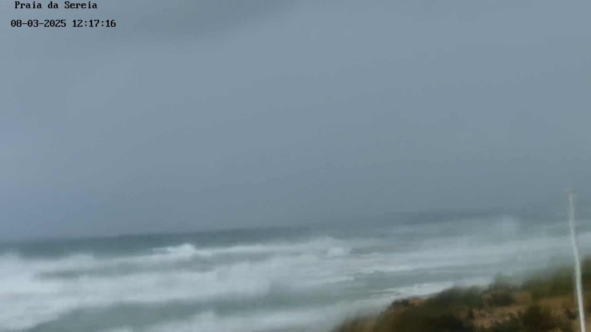 A stormy ocean with choppy waves crashes against a sandy shore under an overcast sky.