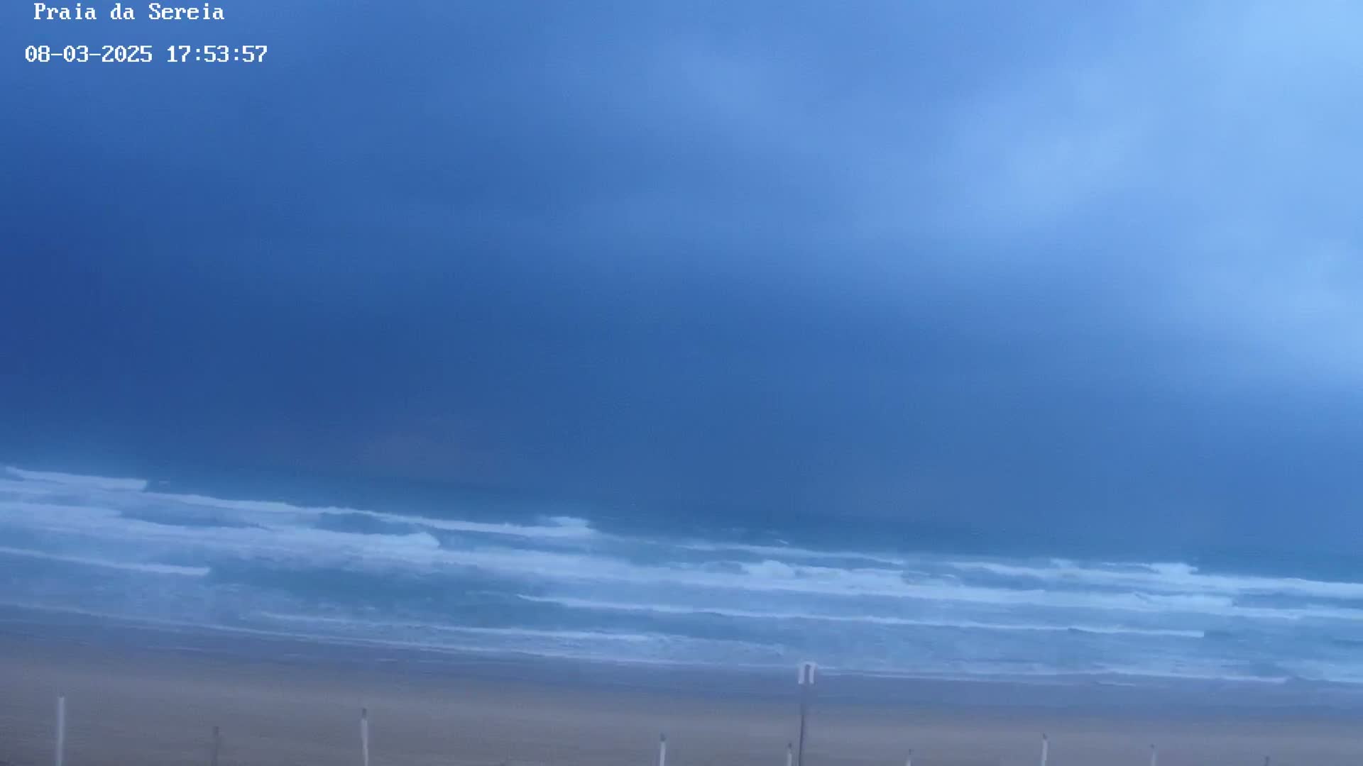 An overcast sky hangs over a beach with waves rolling onto the shore.